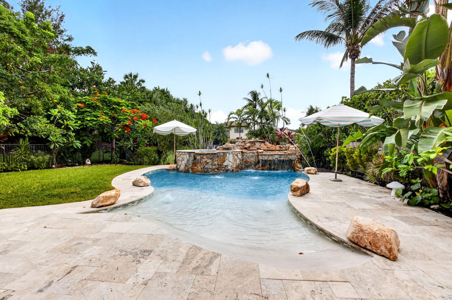 Resort-style pool with a rock waterfall feature, integrated spa, and a natural stone deck