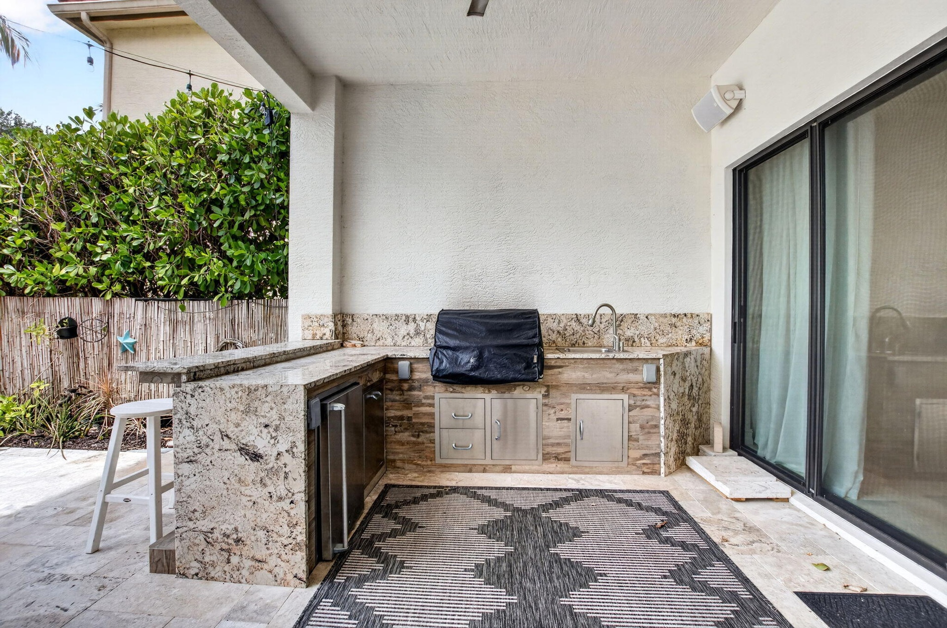 Outdoor kitchen featuring stone countertops, integrated sink, stainless steel under-counter refrigerator, and built-in storage drawers