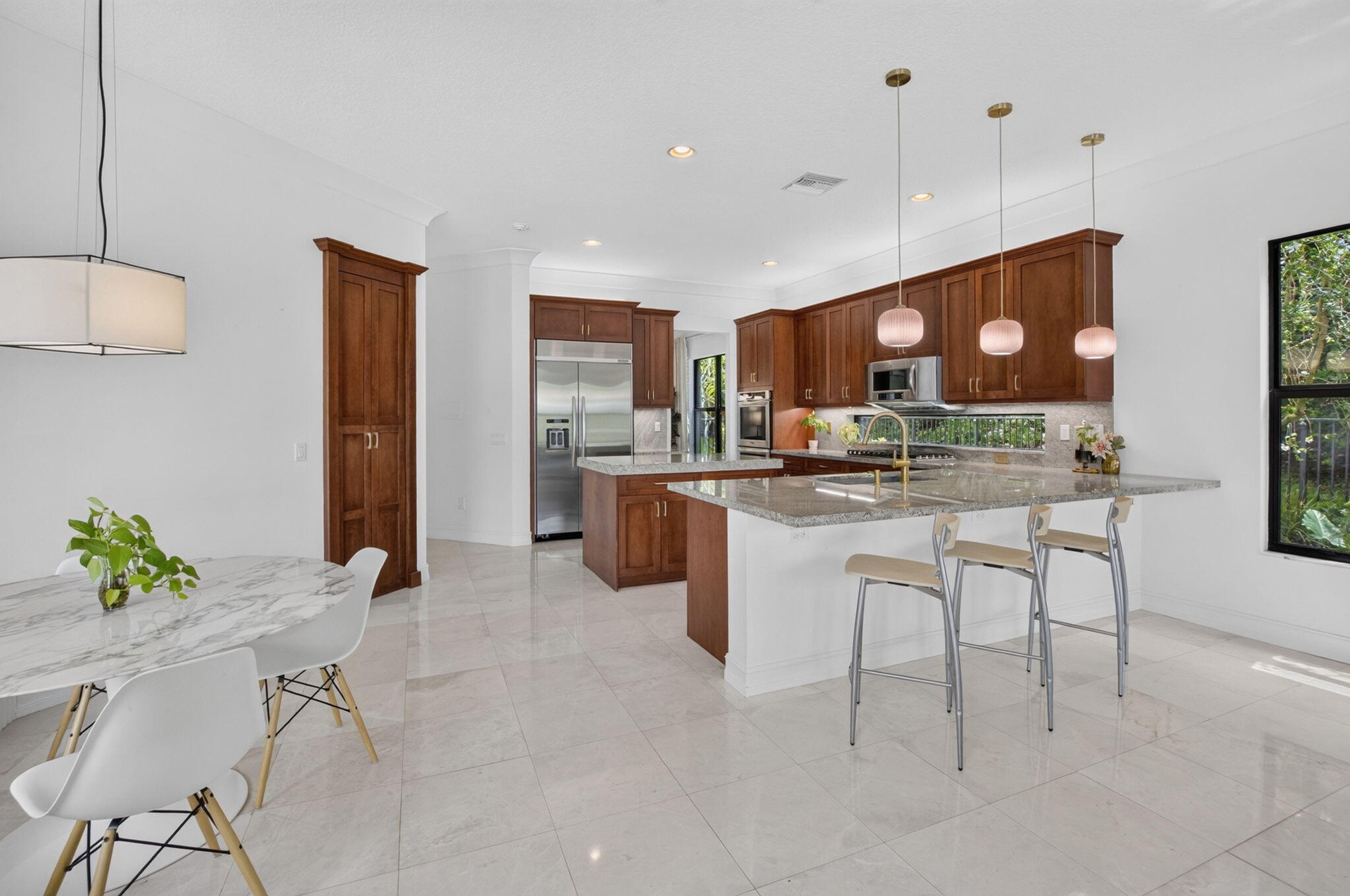 Spacious kitchen featuring warm wood cabinetry, stainless steel appliances, a multi-level island with seating, a window backsplash, and pendant lighti