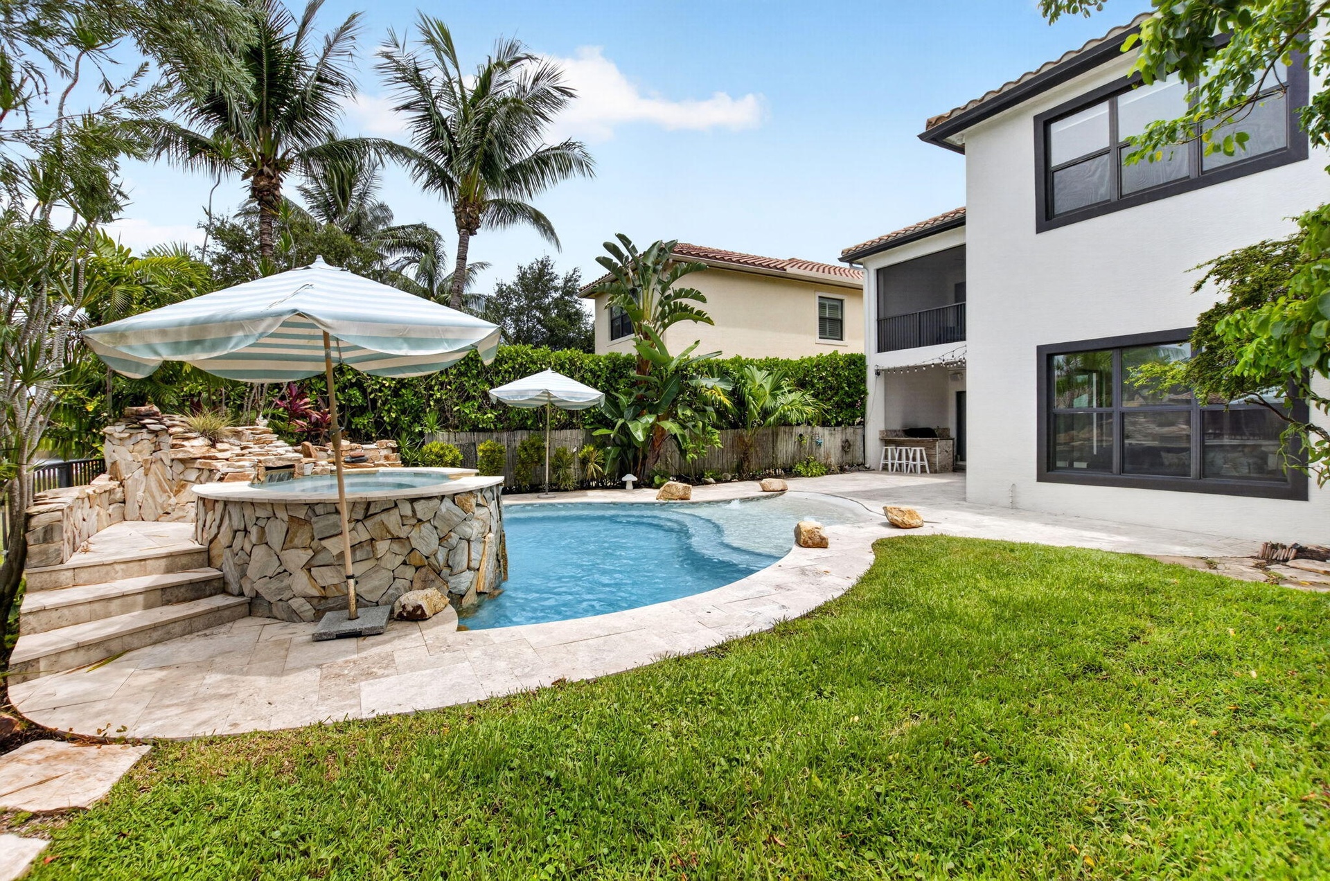Resort-style backyard featuring a freeform swimming pool, integrated spa with stone surround, and a tiered rock waterfall