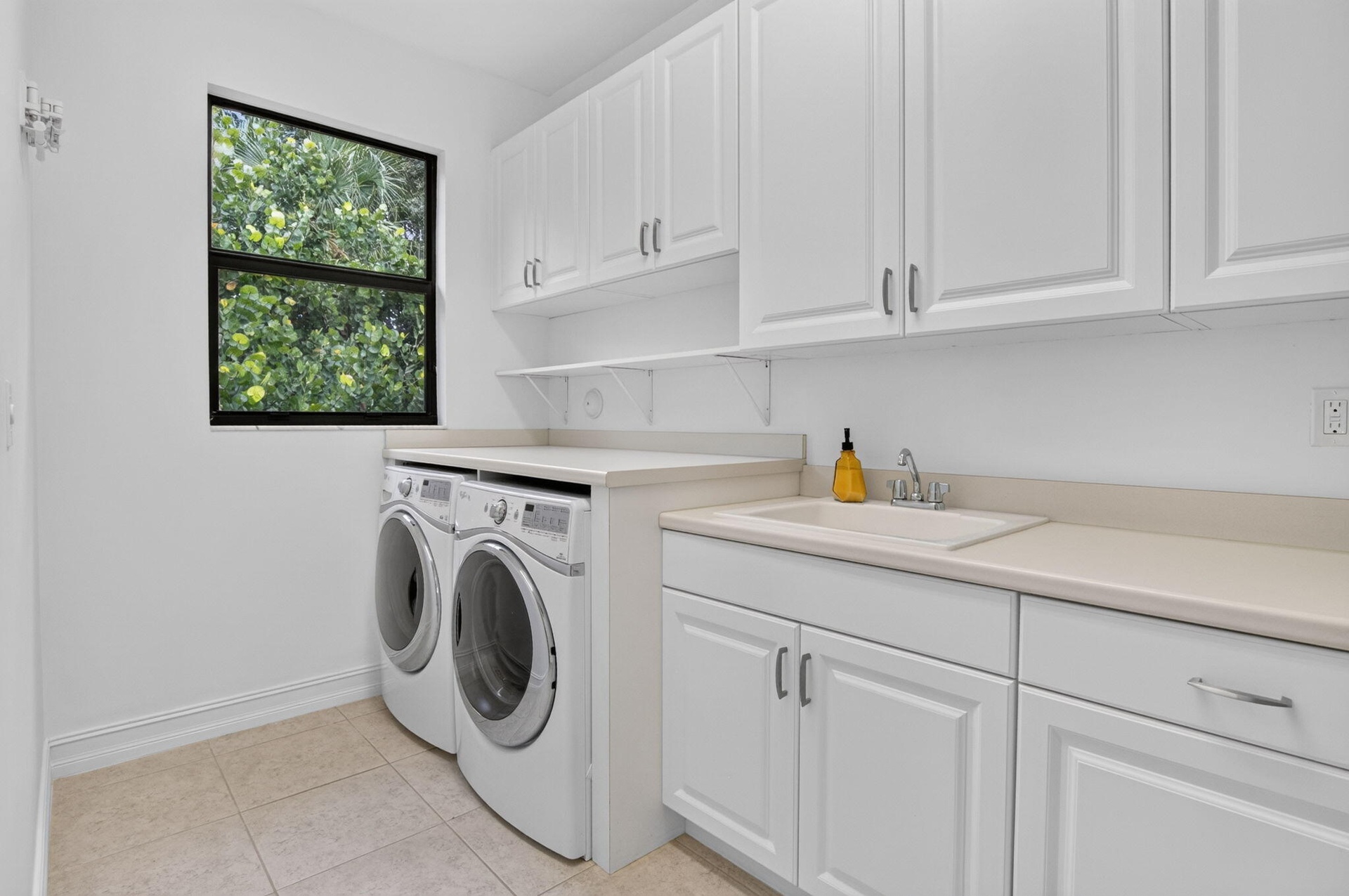 Dedicated utility room featuring white shaker-style cabinetry, a built-in utility sink, light-toned countertops, and a window providing natural light