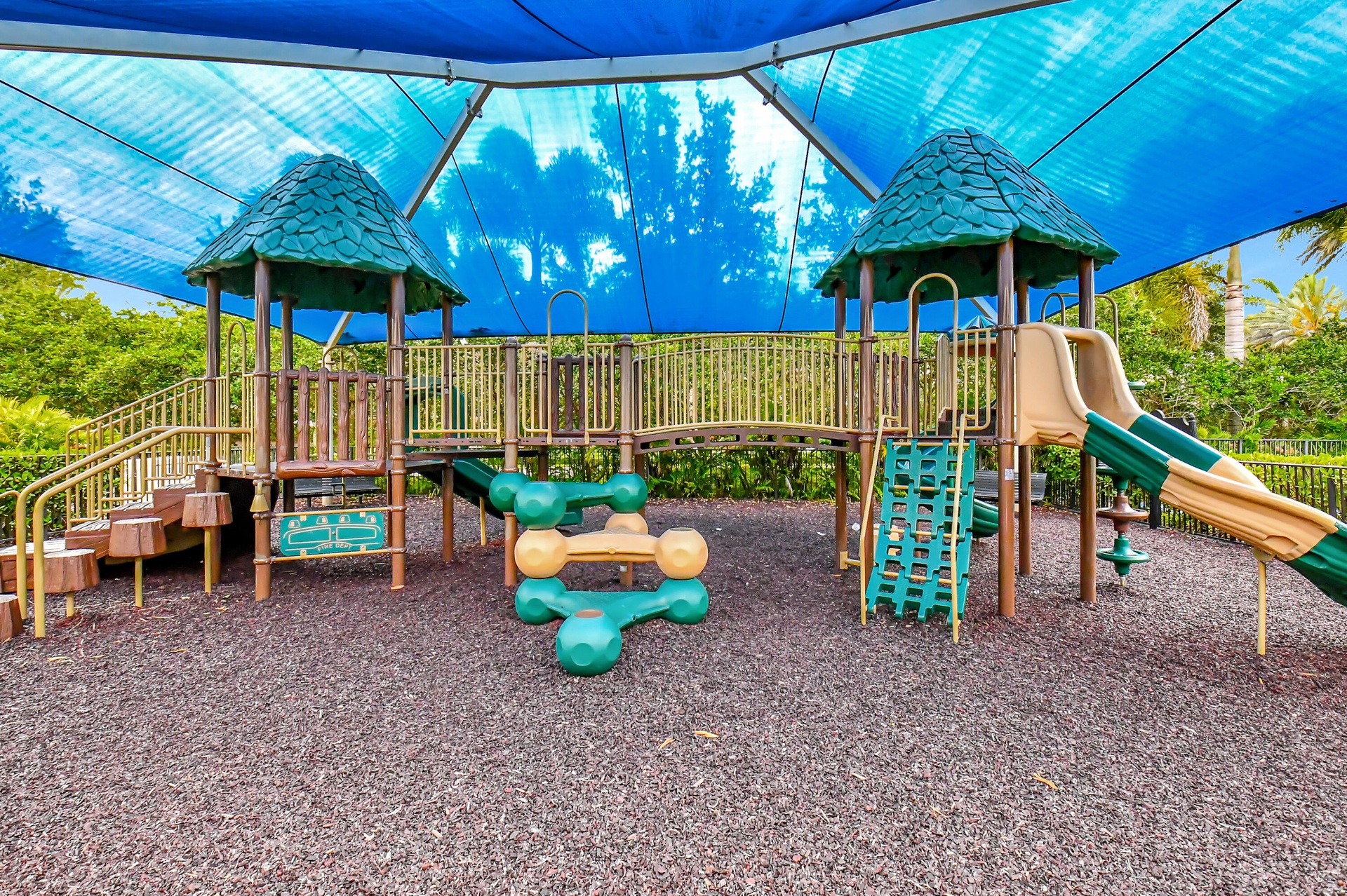 Playground structure with multiple slides and climbing elements, set on a dark-toned impact-absorbing surface