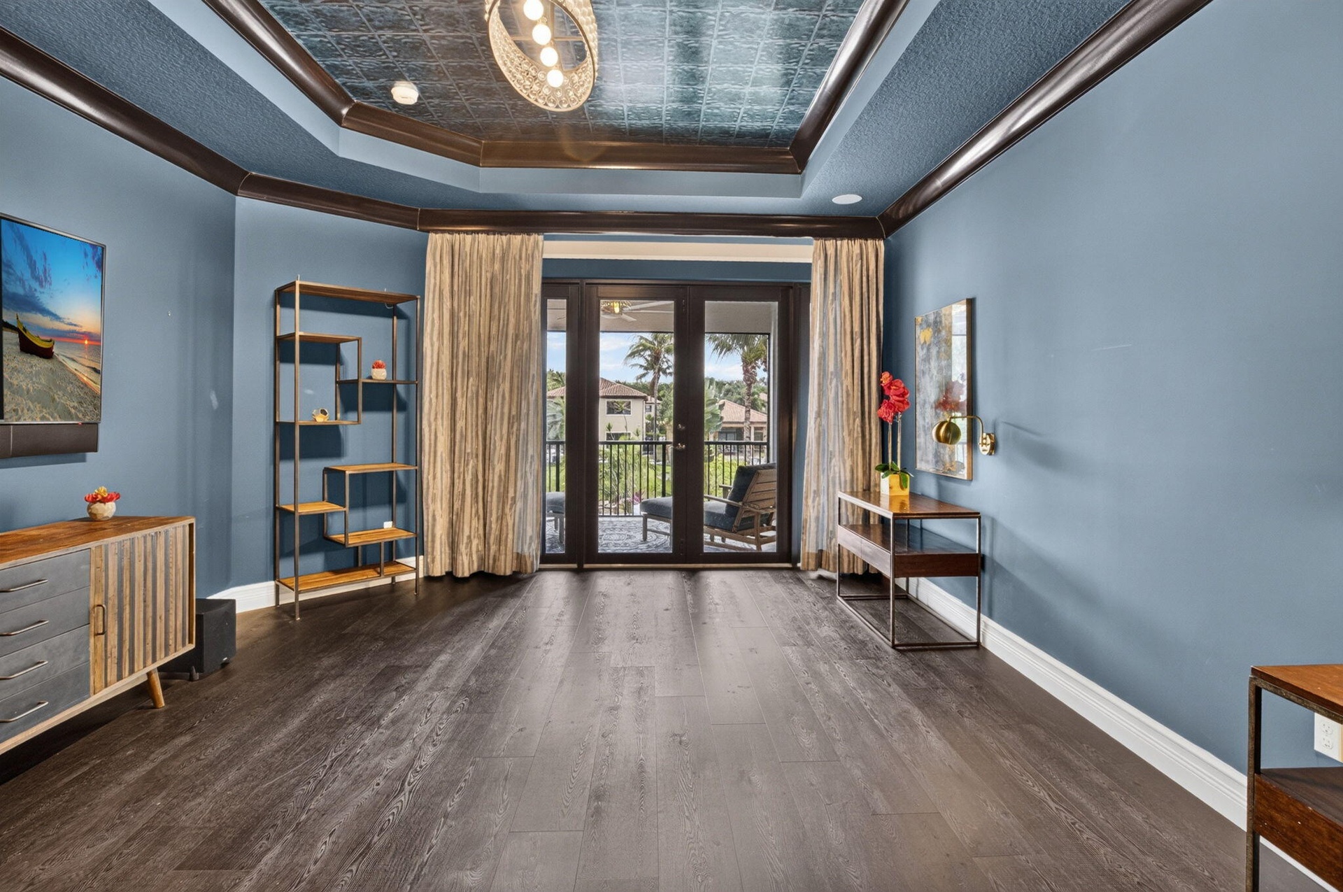 Spacious room featuring dark wood-finish flooring, blue walls, and a decorative ceiling with a central chandelier