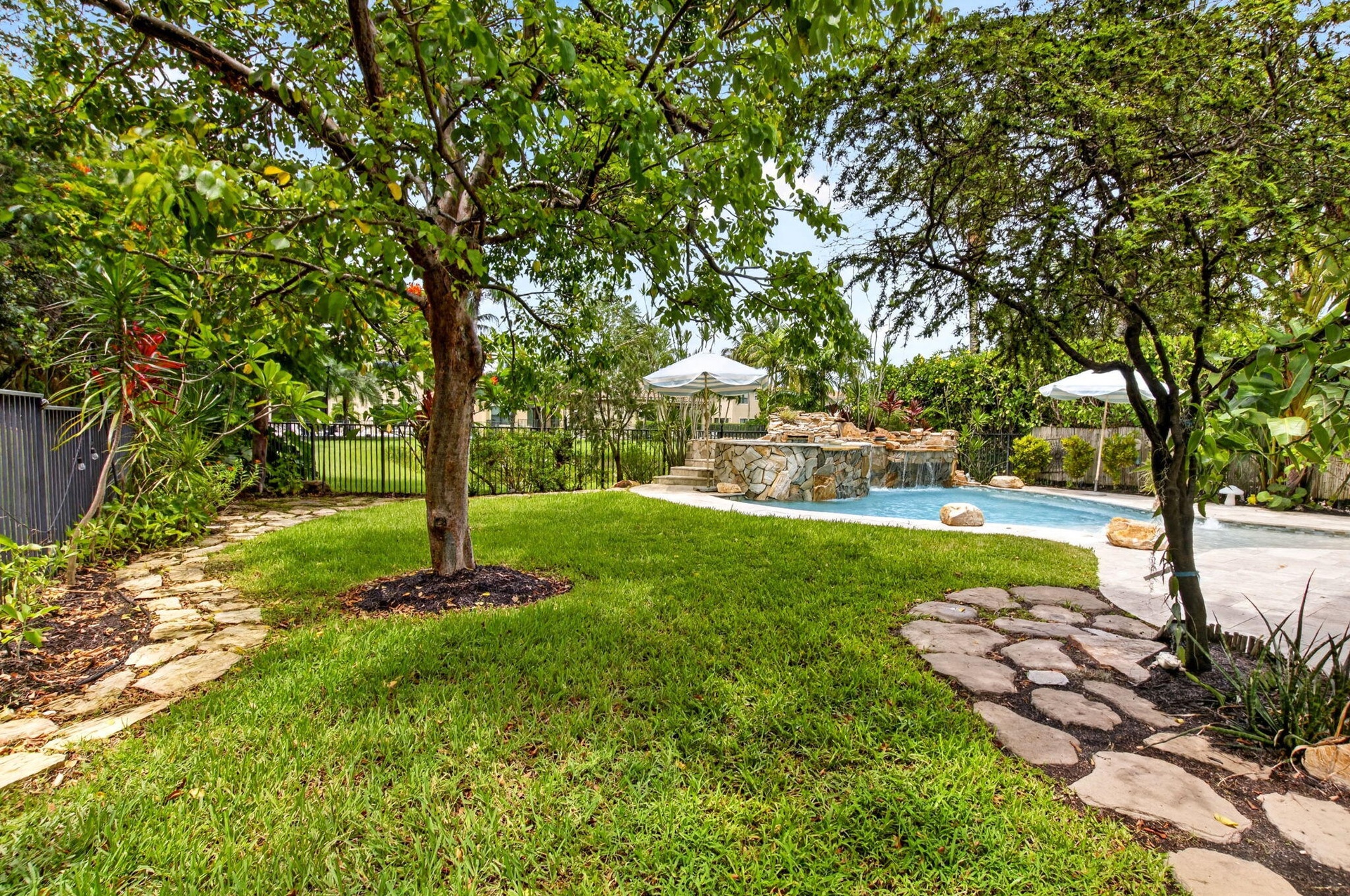 Expansive backyard featuring a lush lawn, mature trees, and natural stone pathways