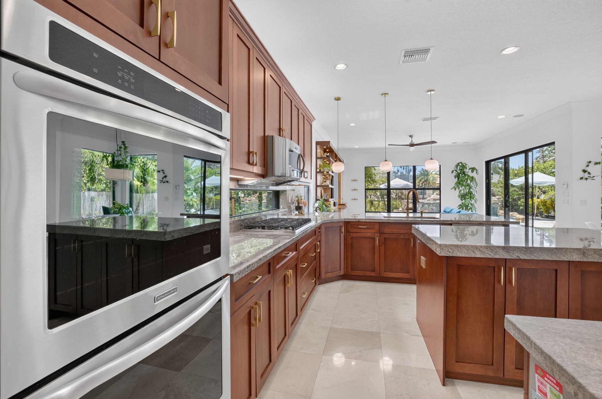 Gourmet kitchen featuring stainless steel double ovens, rich wood cabinetry with gold-tone hardware, light-toned stone countertops, and recessed light