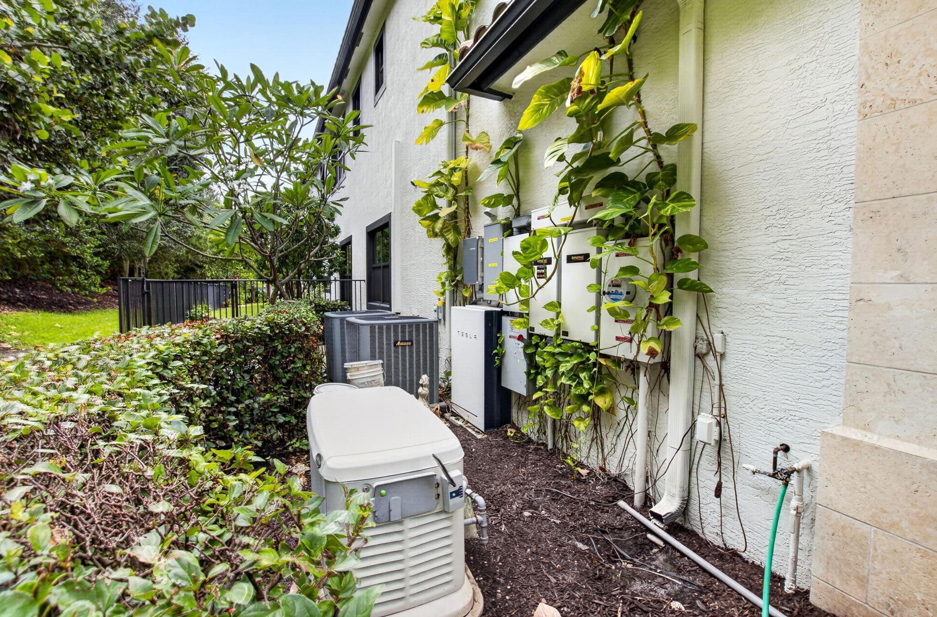 Exterior utility area featuring a standby generator, multiple electrical panels, and air conditioning units