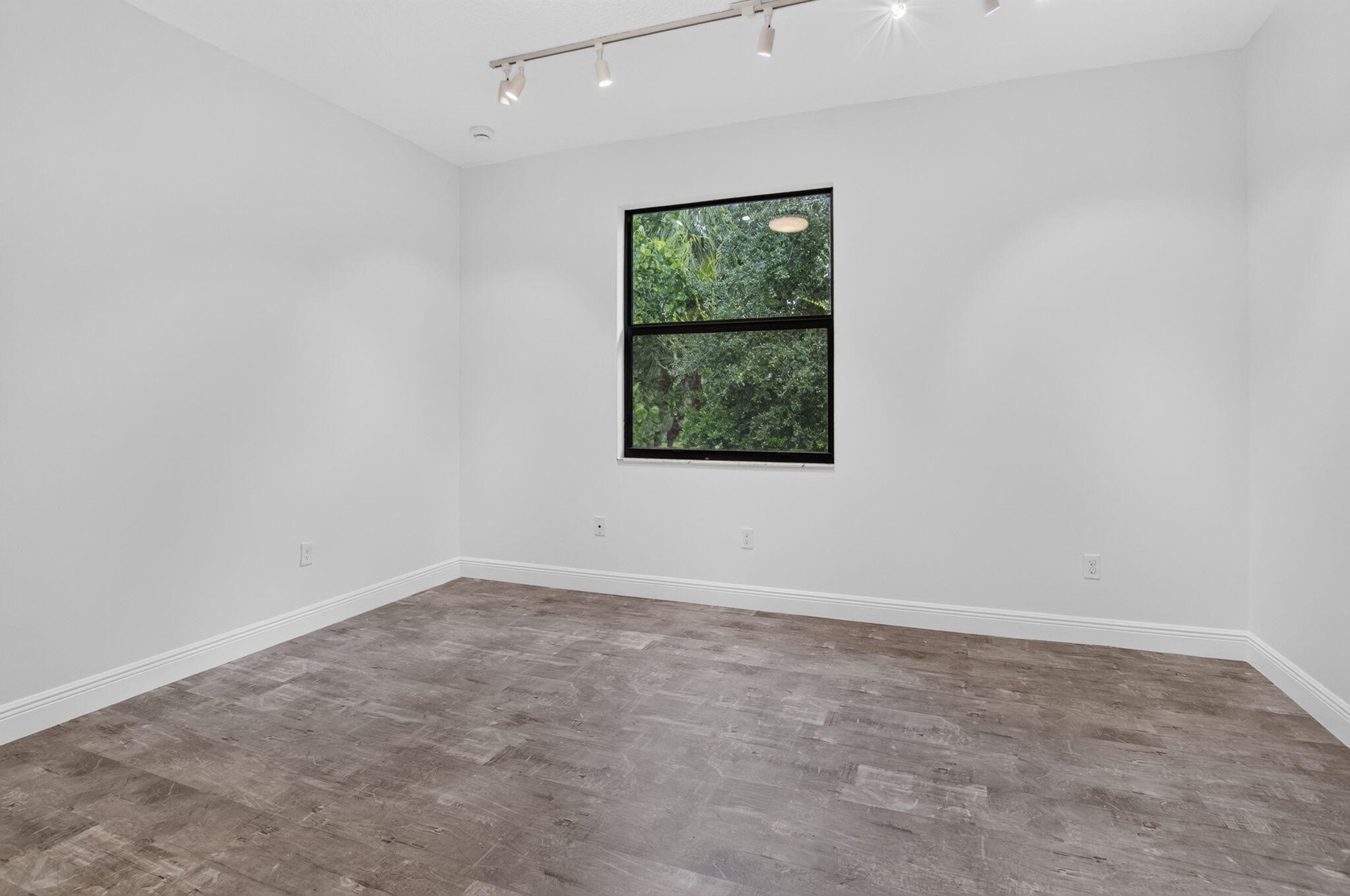 Spacious room featuring wood-finish flooring, white walls, and a black-framed window