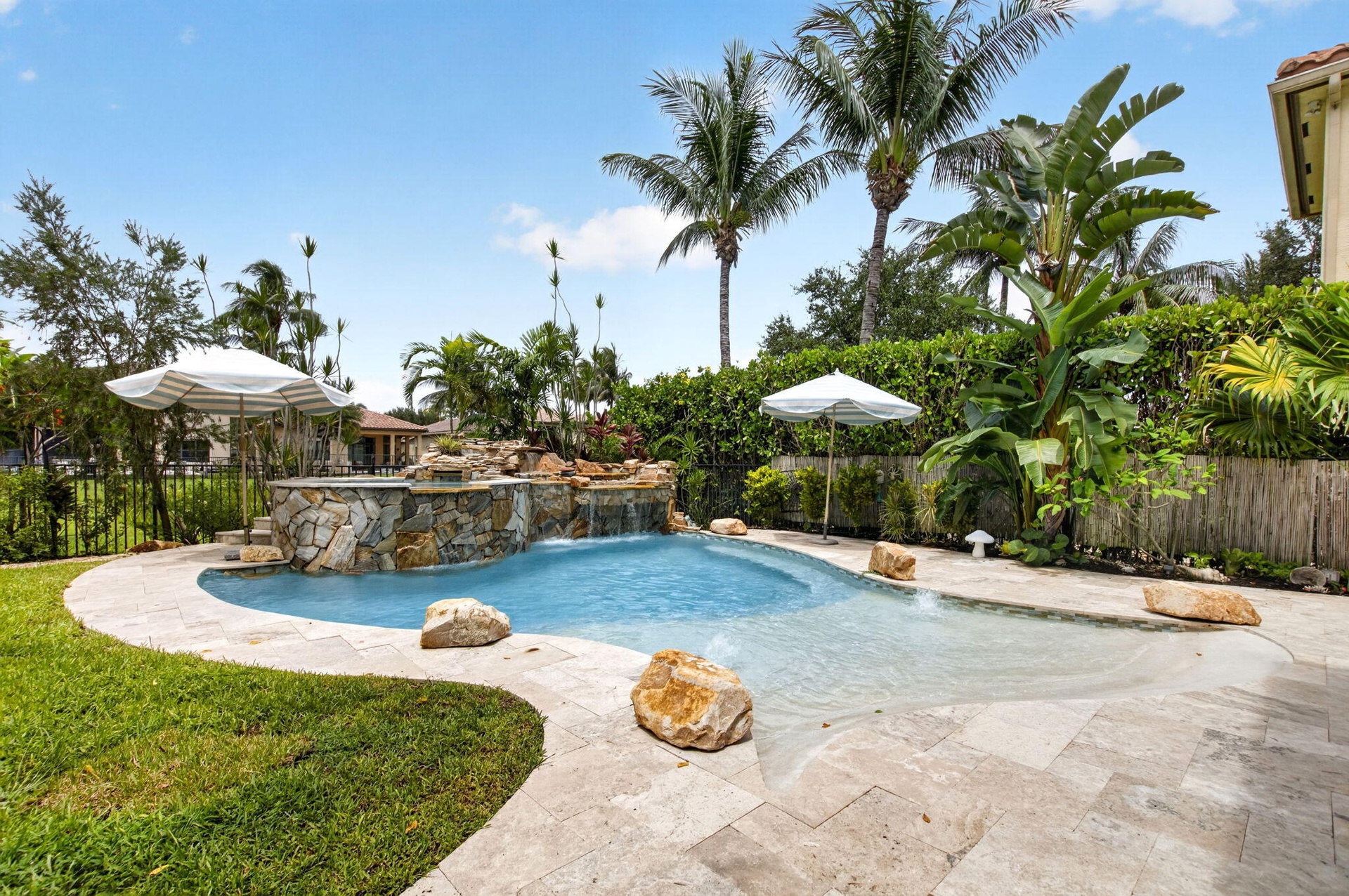 Curved swimming pool featuring a rock waterfall, sun shelf, and paver decking