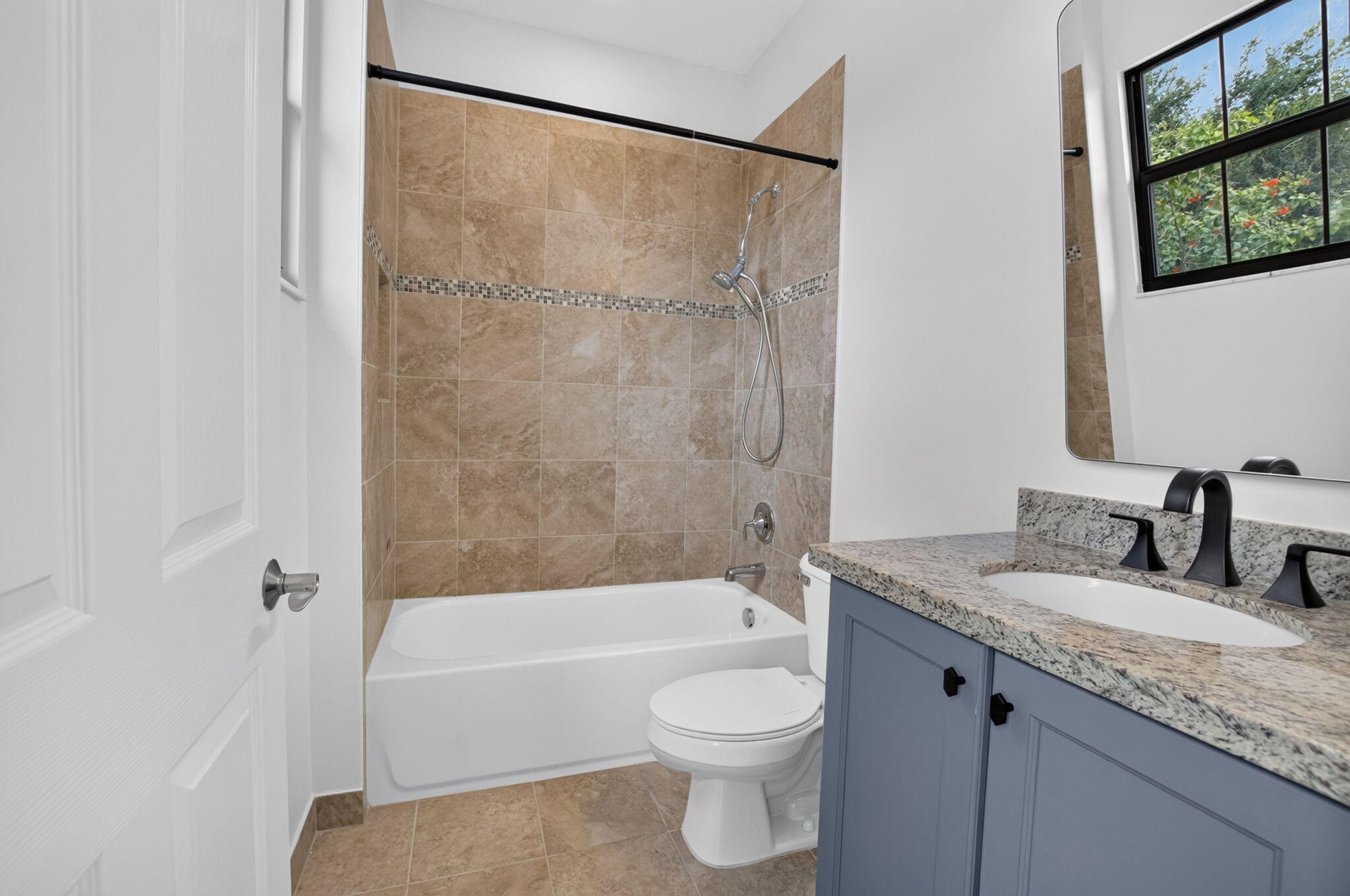 Bathroom featuring a tub/shower combination with tile surround and decorative accent band, a single vanity with granite countertop and undermount sink