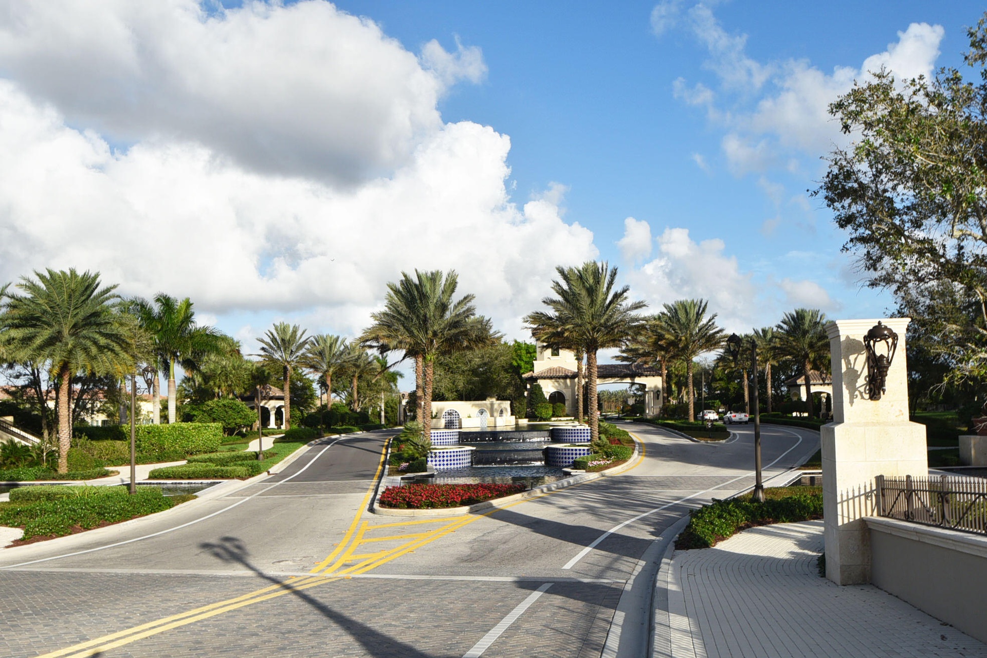 Paved entryway featuring a multi-tiered fountain and lush tropical landscaping