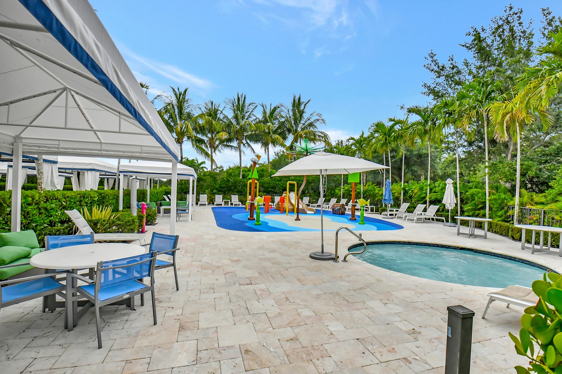Expansive outdoor amenity space featuring a hot tub, a dedicated splash pad with water features, multiple shaded cabanas, and a surrounding patio with