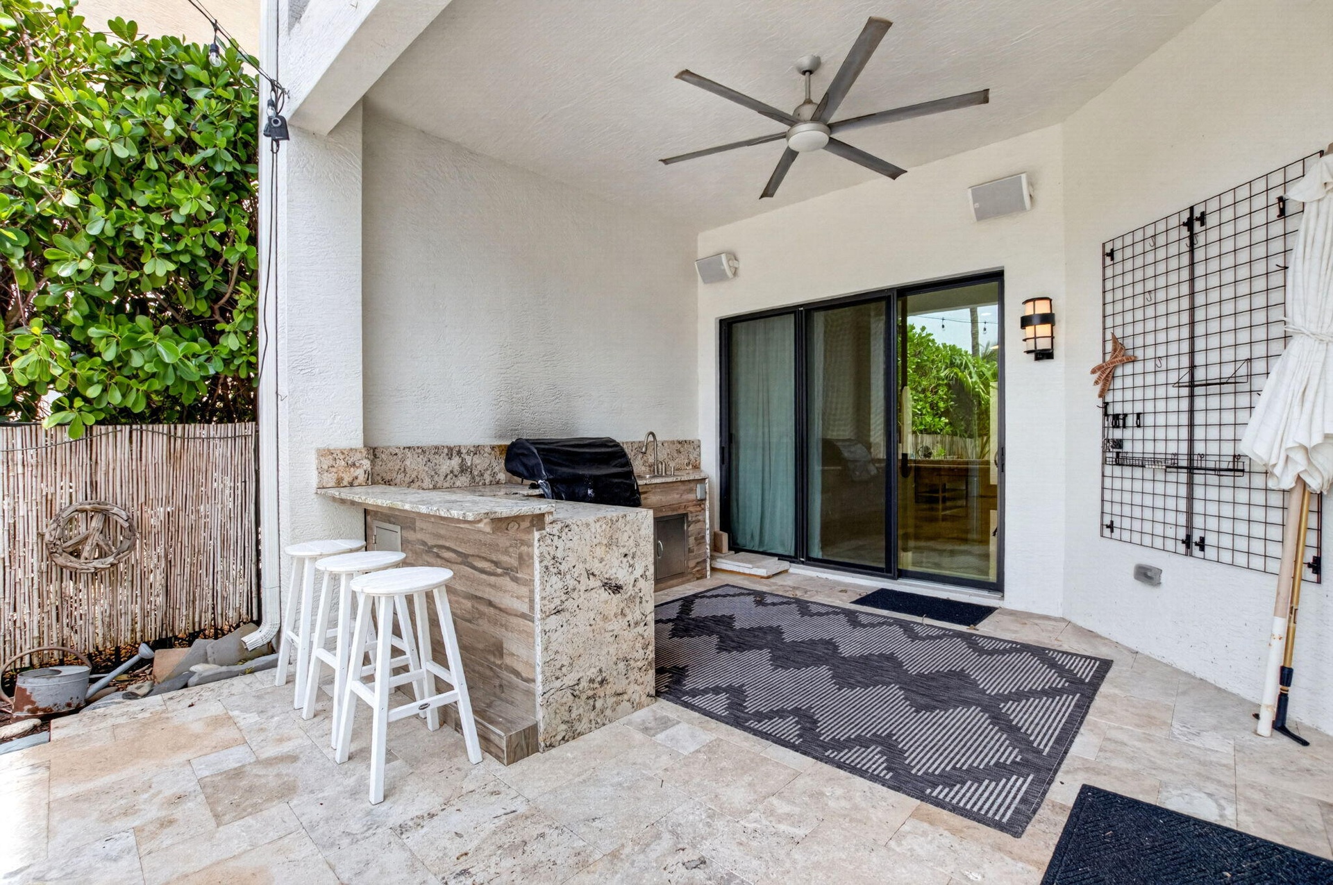 Covered outdoor patio featuring a built-in outdoor kitchen with stone-finish countertops, a ceiling fan, and sliding glass doors
