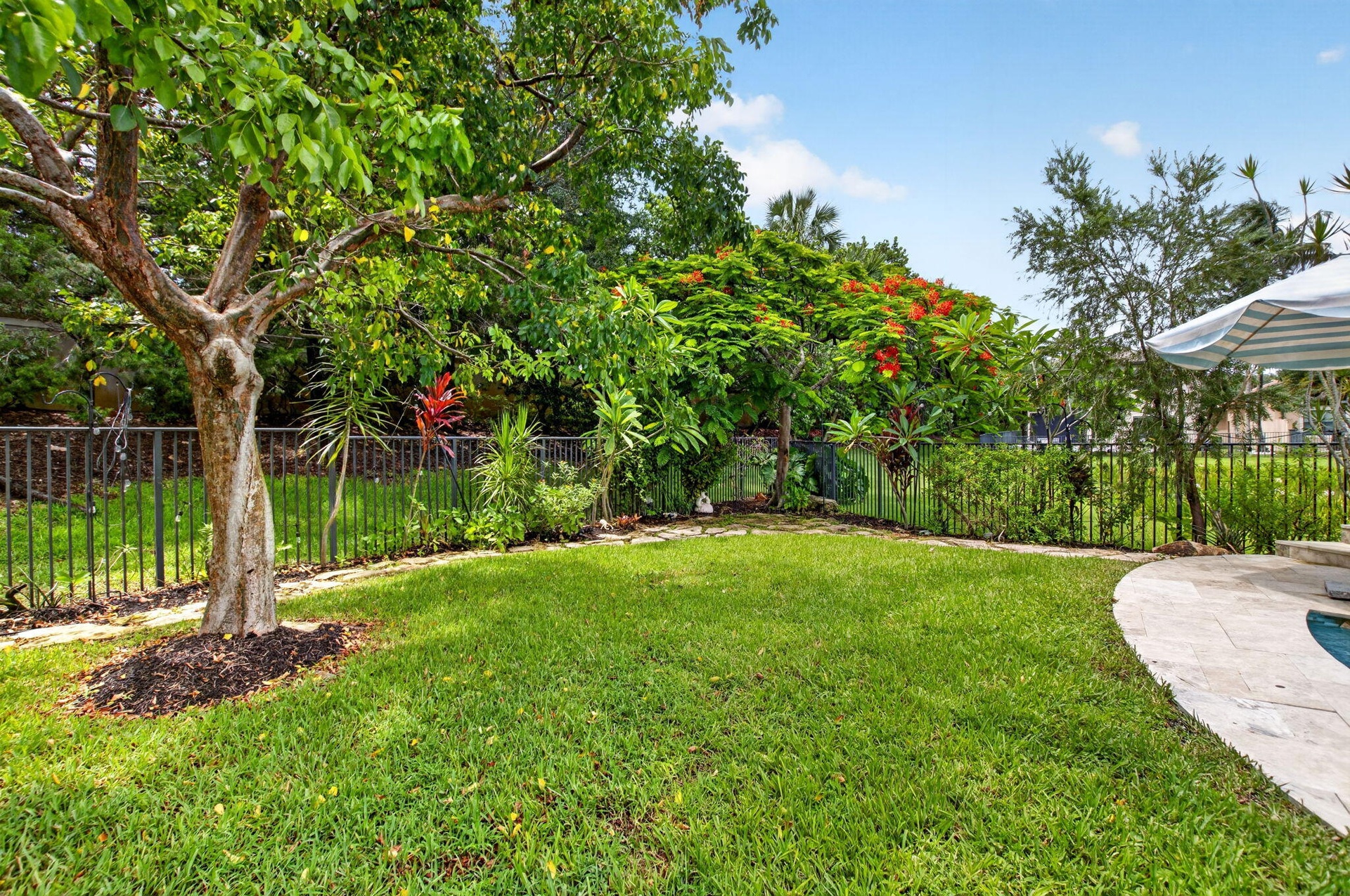 Spacious backyard featuring a lush lawn, mature trees, and a black wrought iron fence