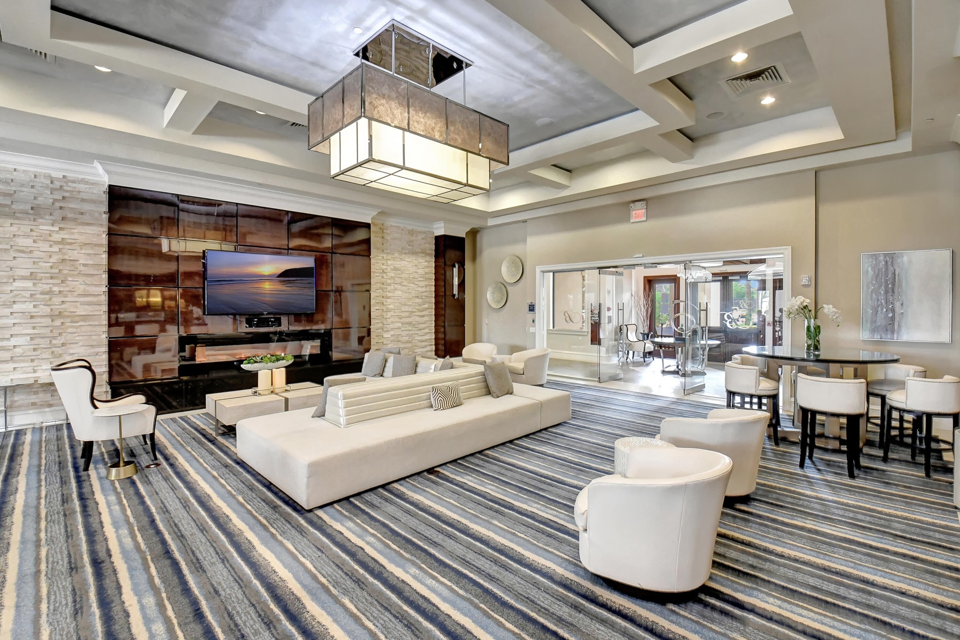 Spacious room featuring a multi-level coffered ceiling, large rectangular chandelier, and striped floor covering
