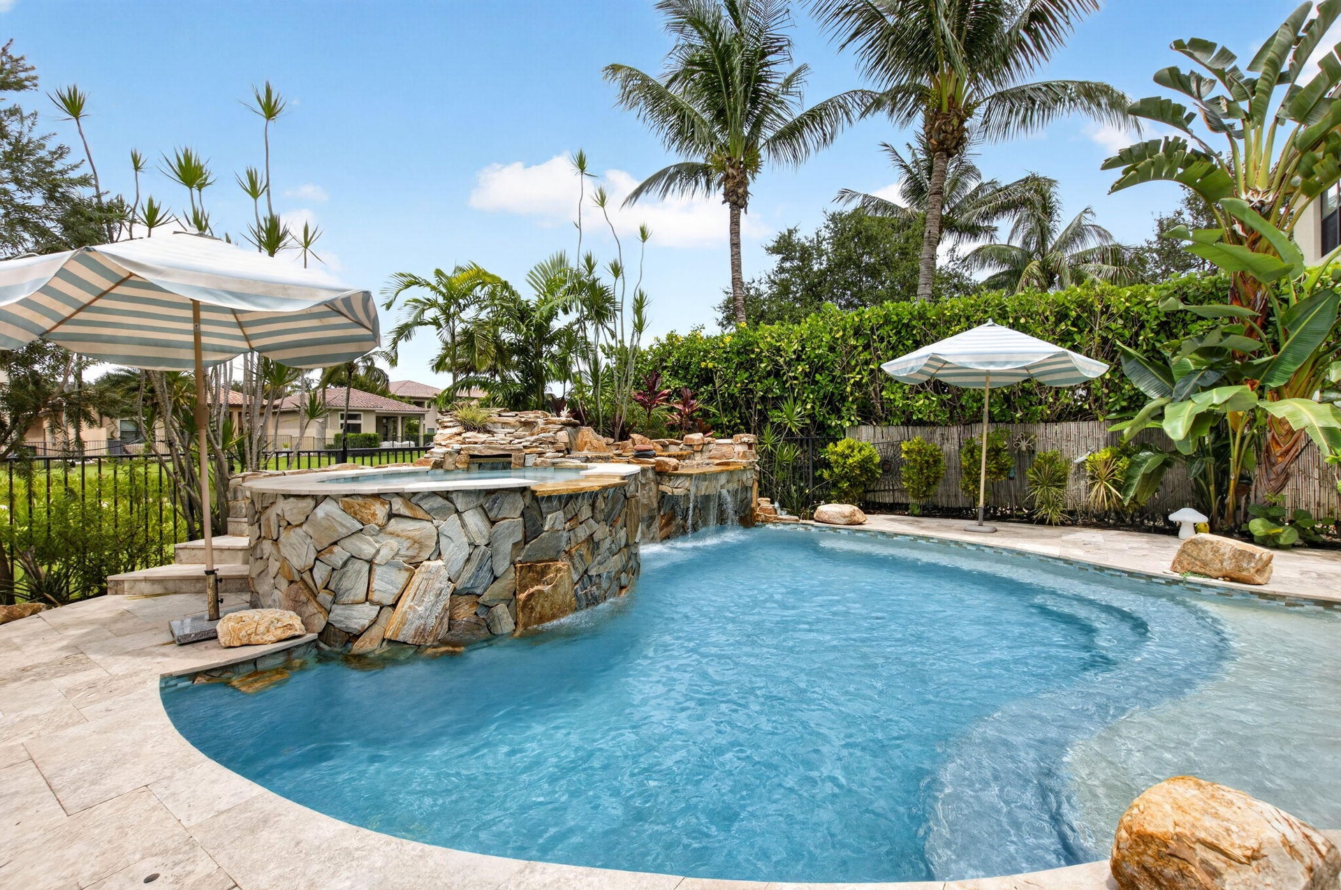 Custom-shaped pool featuring stone coping, an integrated spa with stone cladding, and a cascading waterfall