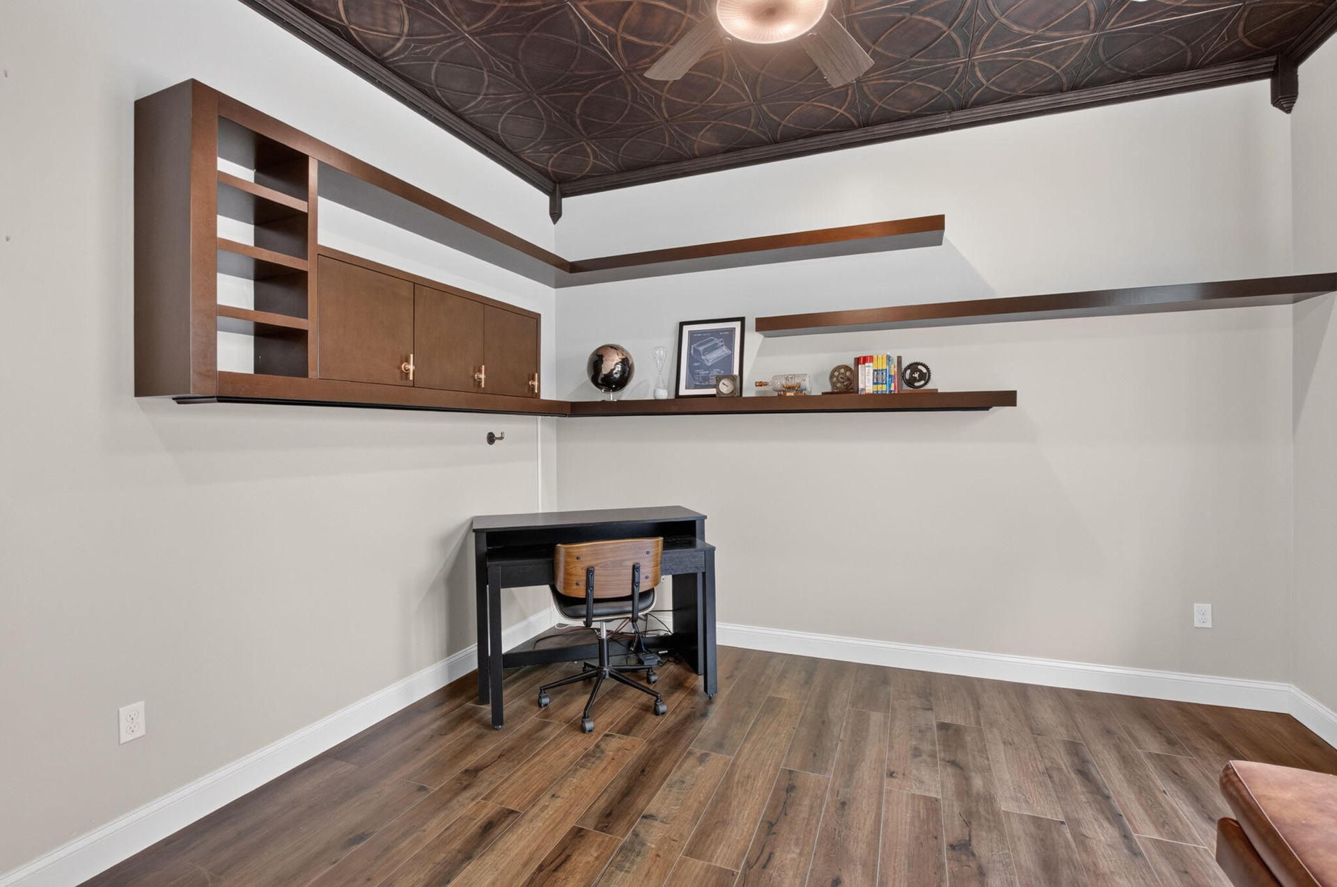 Room featuring wood-finish flooring, a decorative patterned ceiling, and a ceiling fan