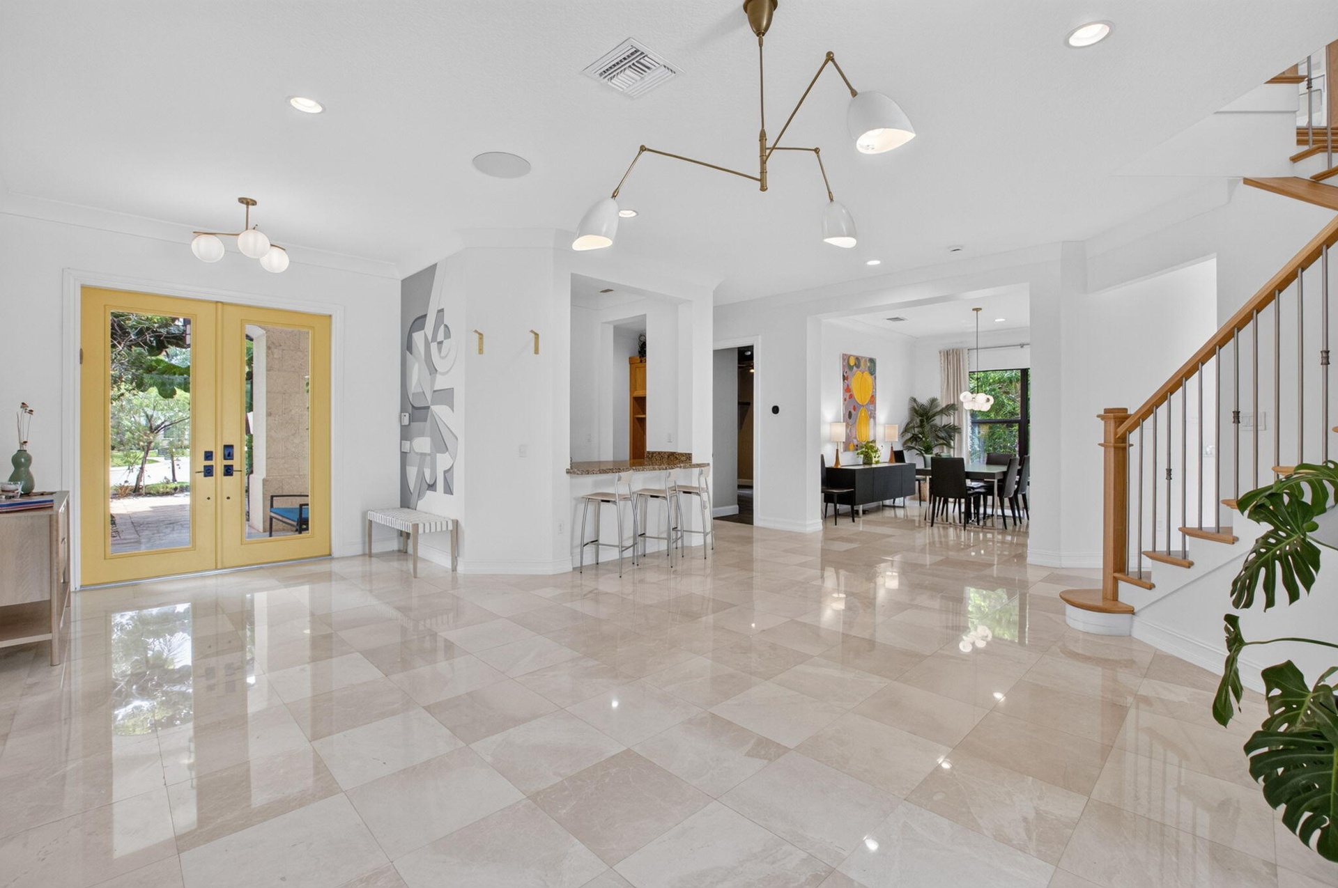 Spacious entry foyer featuring large format tile flooring, a prominent staircase with wood newel posts and metal balusters, and a contemporary chandel