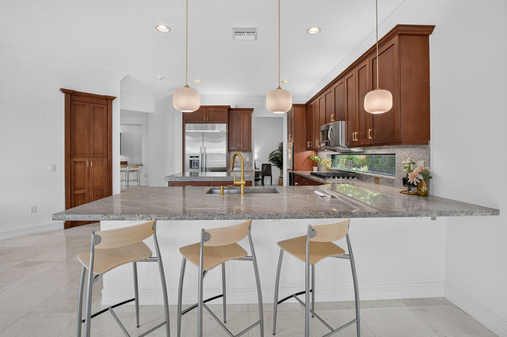 Kitchen featuring an expansive island with a light-toned countertop, warm wood-finish cabinetry, stainless steel appliances, and under-cabinet lightin