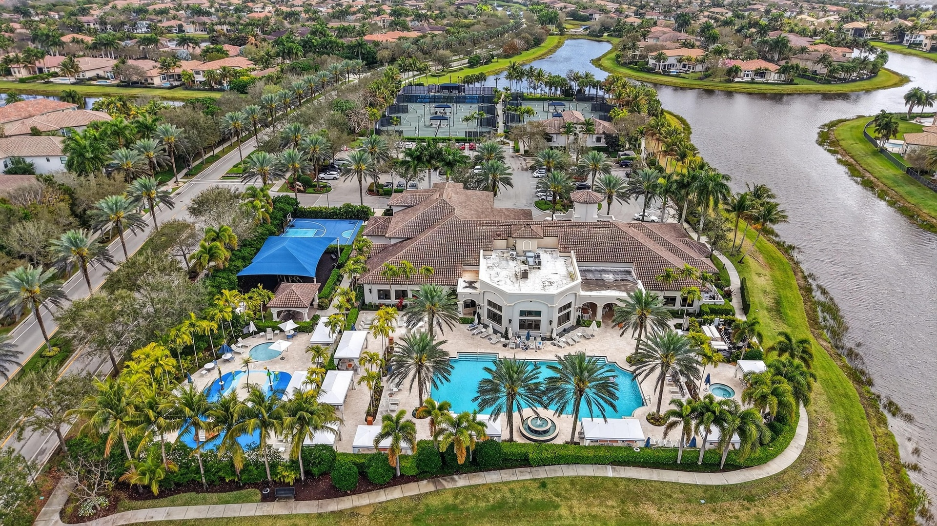 Extensive community amenities featuring multiple swimming pools, a central clubhouse building, tennis courts, and surrounding waterways