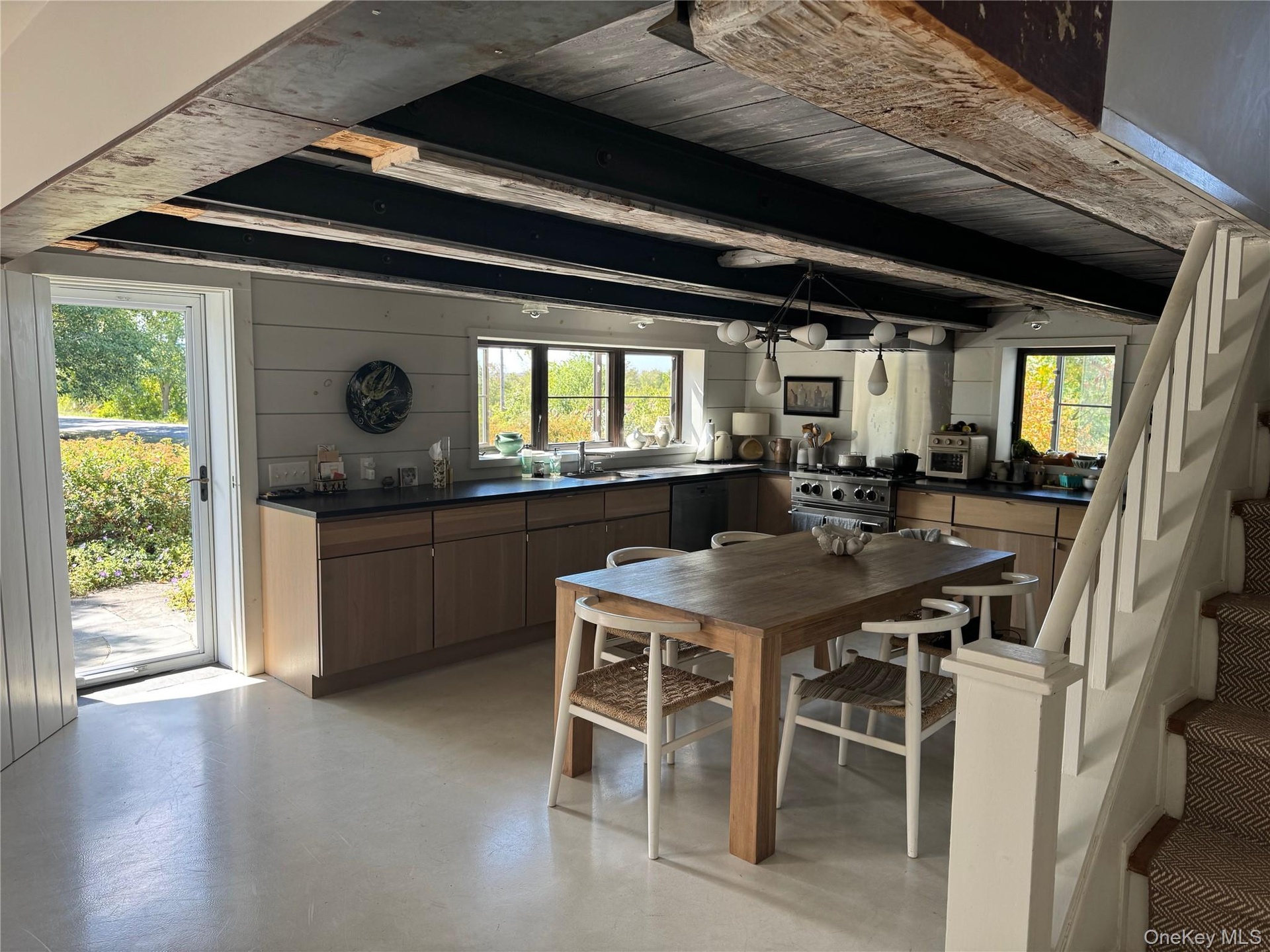 Dining room featuring stairway, beam ceiling, finished concrete flooring, and wooden walls