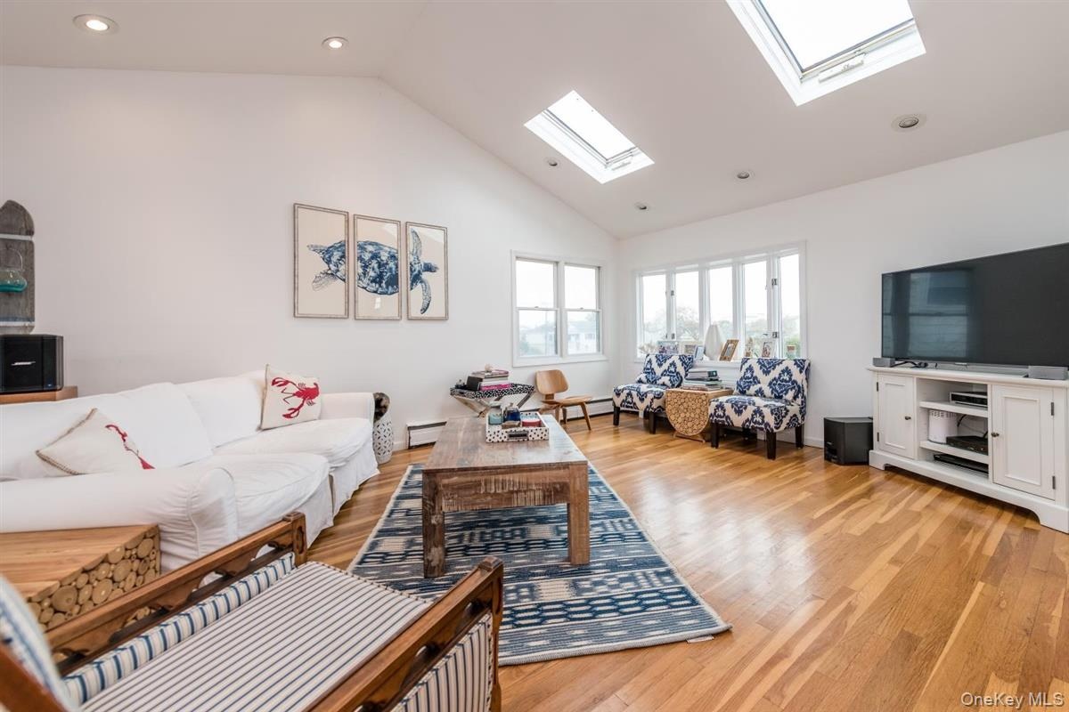 Vaulted ceiling great room featuring recessed lighting, skylights, wood-finish flooring, and multiple windows