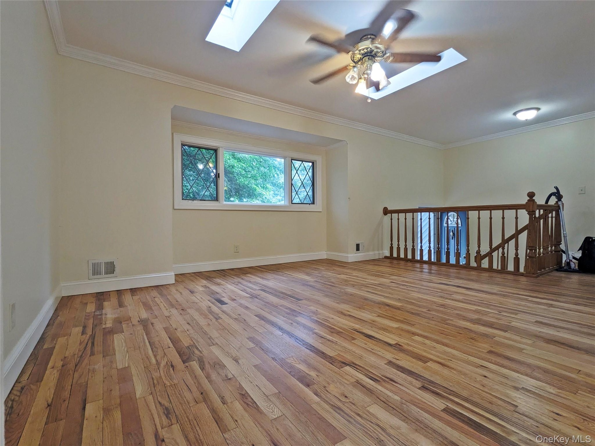 Spacious room featuring wood-finish flooring, a decorative ceiling fan, and two skylights for natural illumination