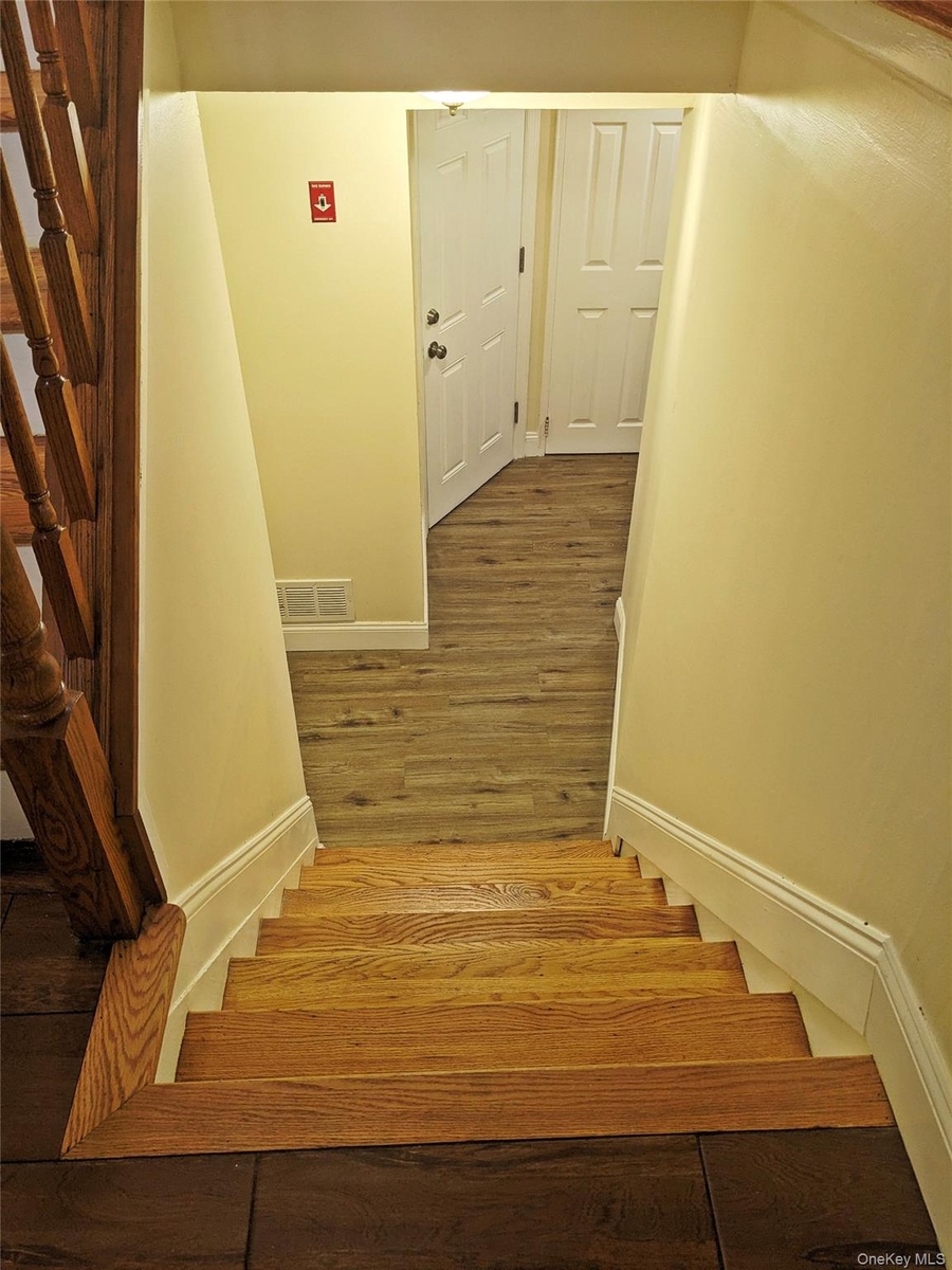Hardwood staircase with natural wood treads and a dark wood newel post leading to a lower level with wood-finish flooring