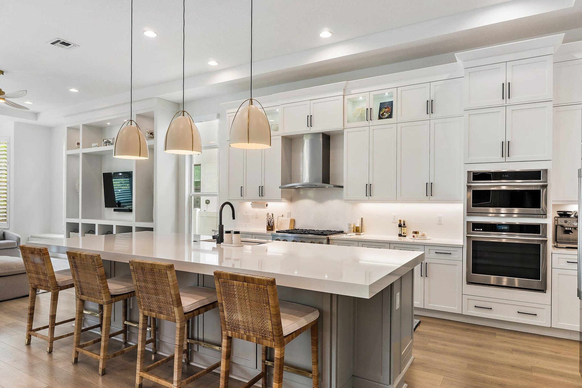 Kitchen with white cabinetry, large island, woven bar stools, and double wall ovens