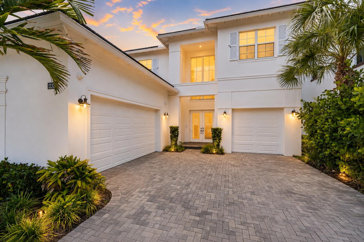 Two-story home exterior with three-car garage and paver driveway at dusk