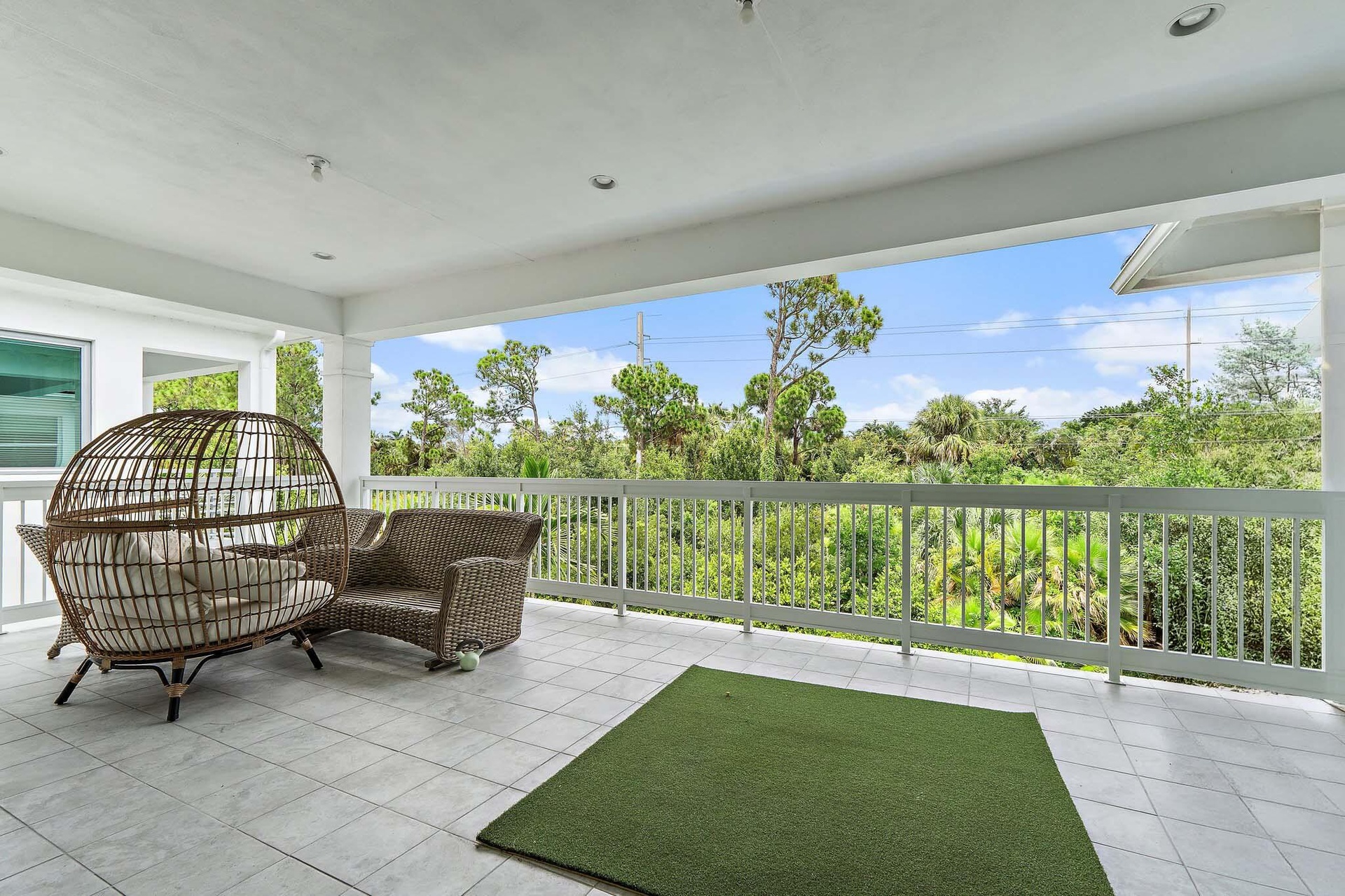 Covered balcony with wicker seating, rug, and tree-lined view