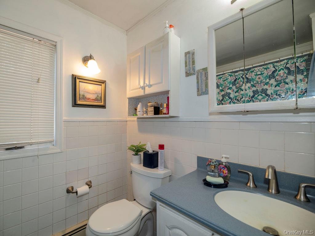 Full bath featuring vanity, crown molding, a baseboard heating unit, tile walls, and a wainscoted wall