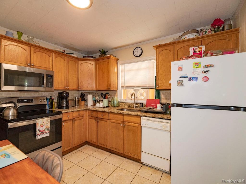 Kitchen featuring appliances with stainless steel finishes, light stone countertops, light tile patterned floors, and brown cabinets