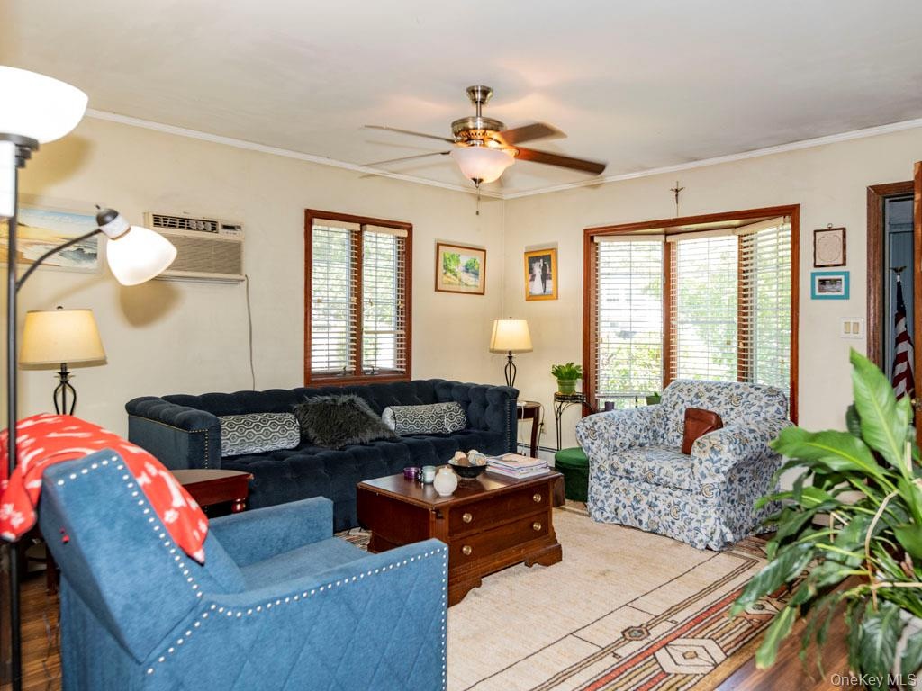 Living area with a ceiling fan, ornamental molding, wood finished floors, and an AC wall unit