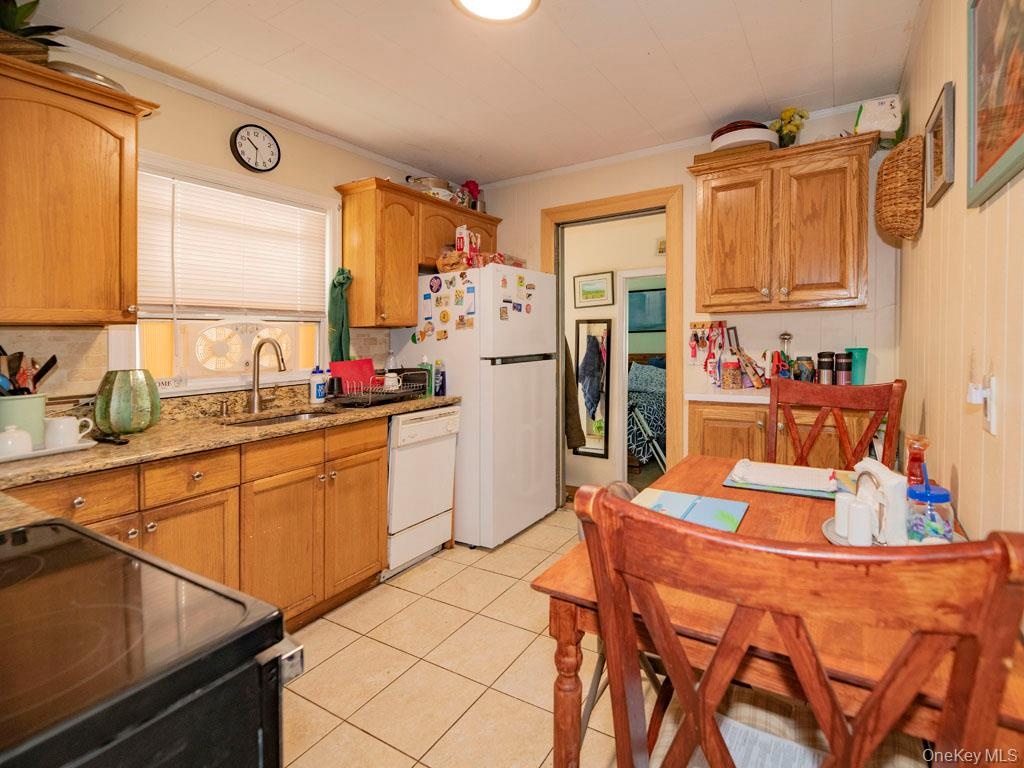 Kitchen featuring white appliances, ornamental molding, light tile patterned flooring, light stone counters, and brown cabinetry
