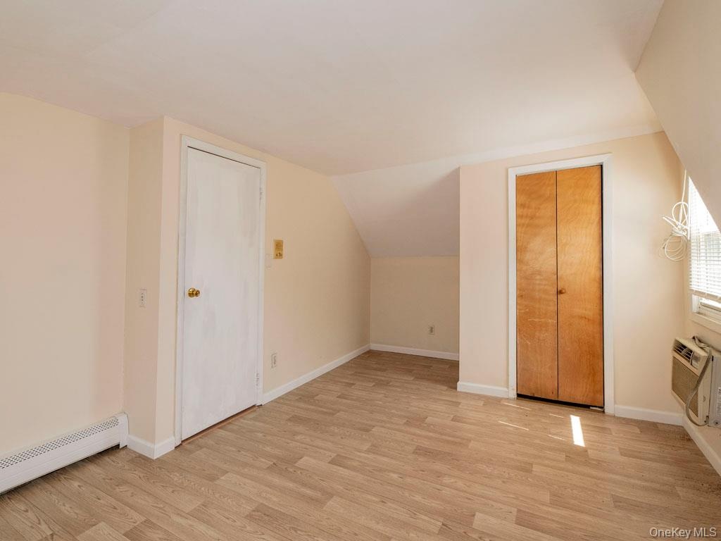 Additional living space featuring light wood finished floors, a baseboard radiator, vaulted ceiling, and an AC wall unit