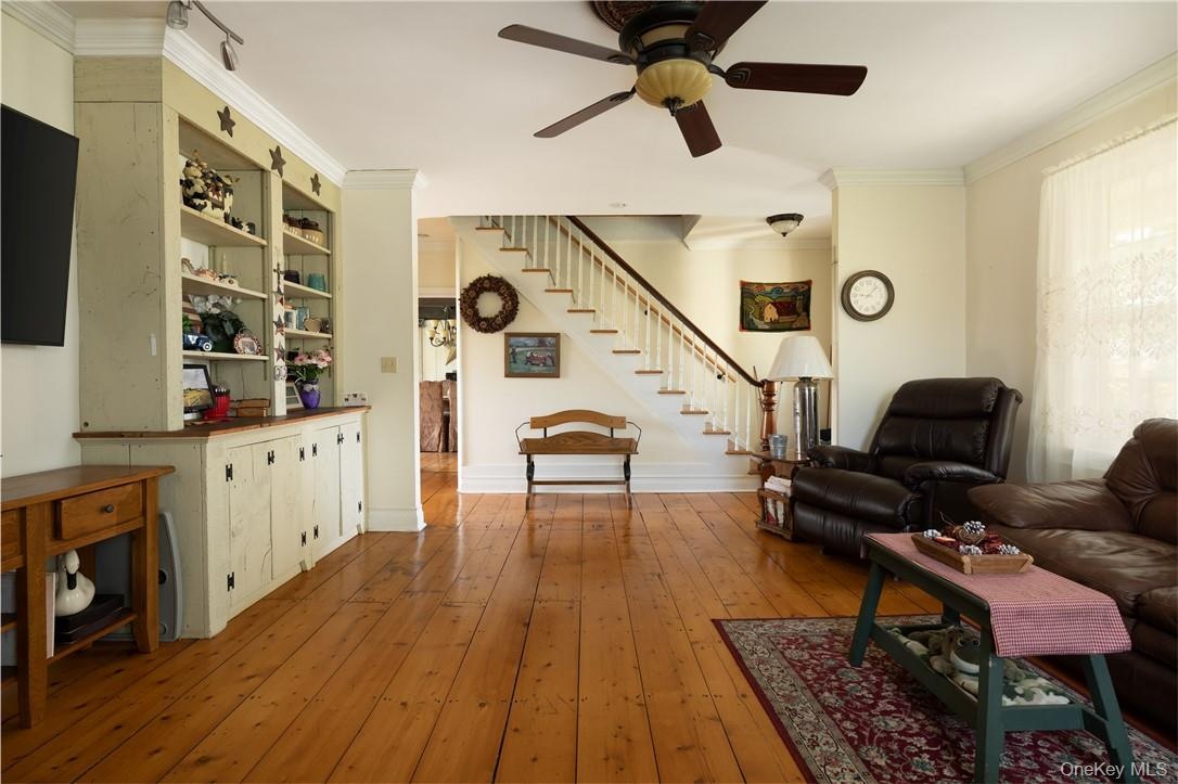 Living room featuring hardwood flooring, crown molding, and ceiling fan