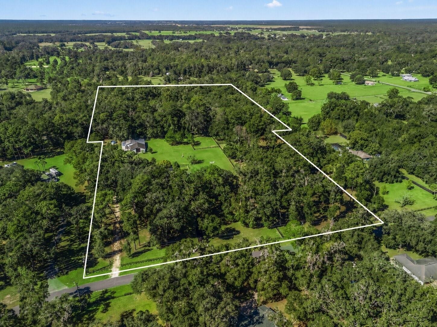 Aerial view of the property highlighting the boundary lines, mature trees, expansive acreage, and private setting.