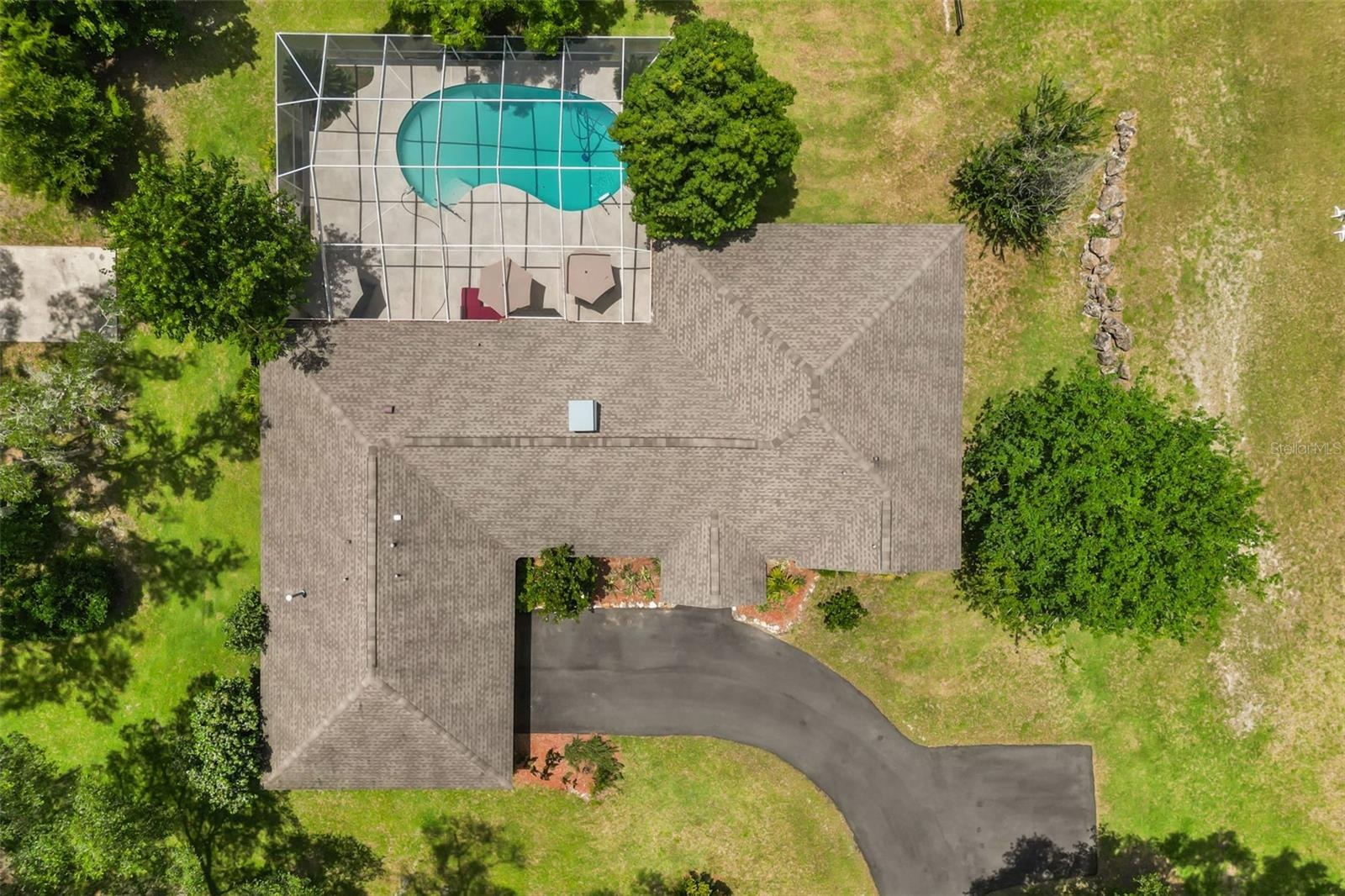 Overhead aerial view showcasing the home's layout, screened pool enclosure, paved driveway, and expansive grounds.