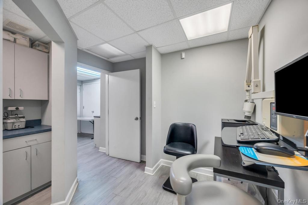 Professional workspace featuring light gray walls, wood-finish flooring, and a suspended ceiling with integrated lighting