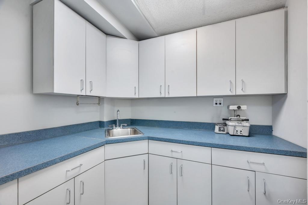 Corner workstation featuring extensive white cabinetry, speckled blue countertops, and an integrated stainless steel sink with a chrome faucet
