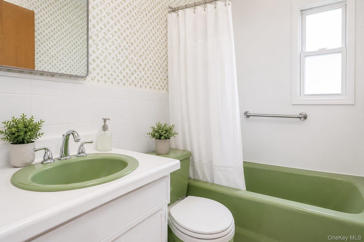 Bathroom featuring a green drop-in sink, white vanity, white tile wainscoting, green bathtub, and a window providing natural light