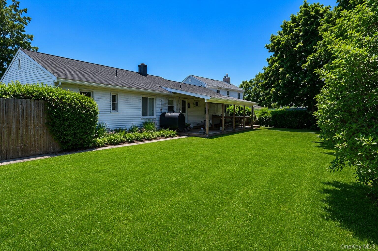 Expansive lawn with a covered deck, mature perimeter plantings, and a wooden privacy fence