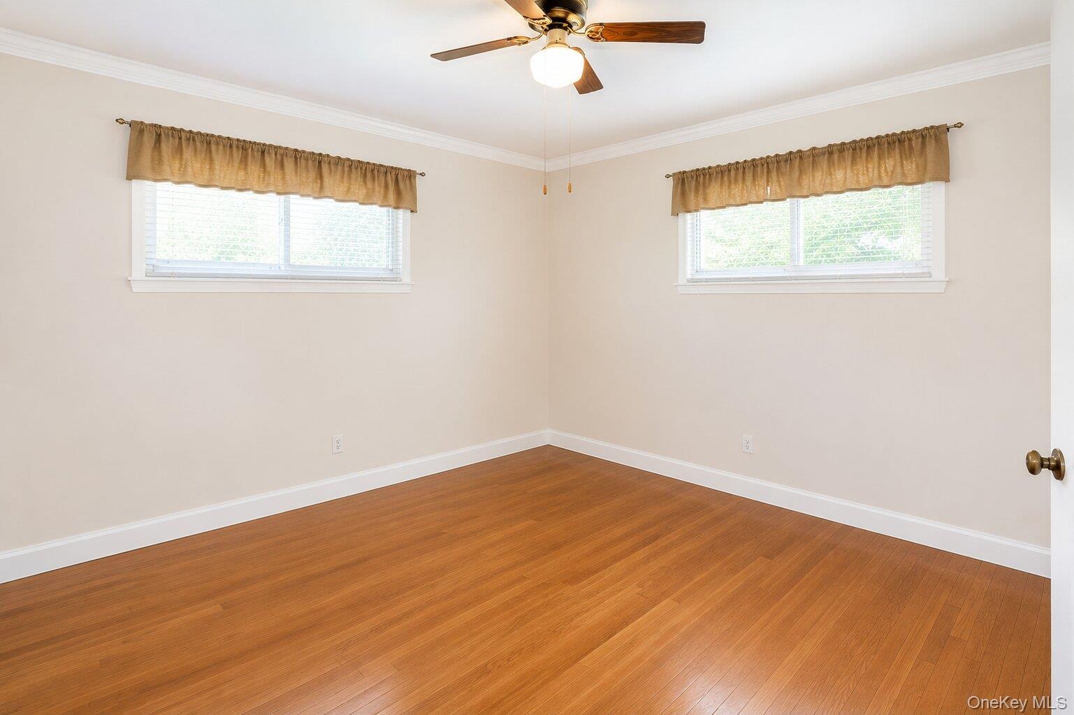 Room featuring wood-finish flooring, white baseboards, and white crown molding