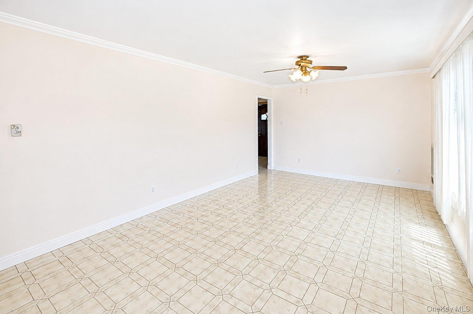 Spacious room featuring geometric tile flooring, crown molding, baseboards, and a ceiling fan with integrated lighting