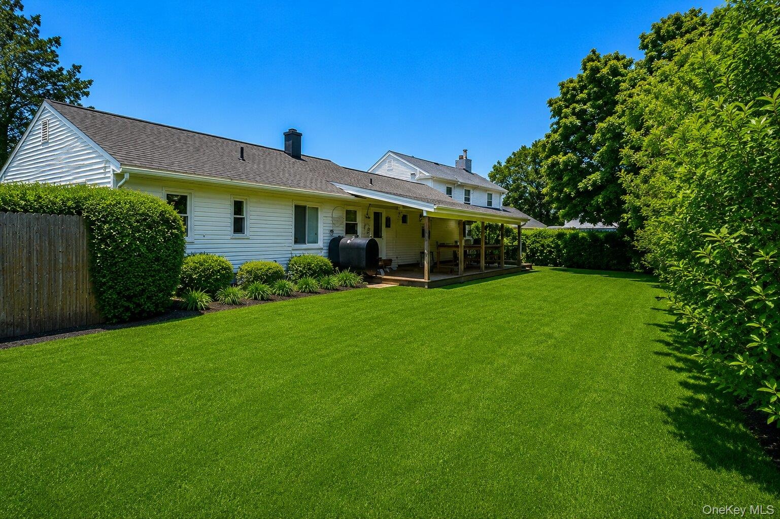 Expansive green lawn with a covered wood deck and mature perimeter landscaping
