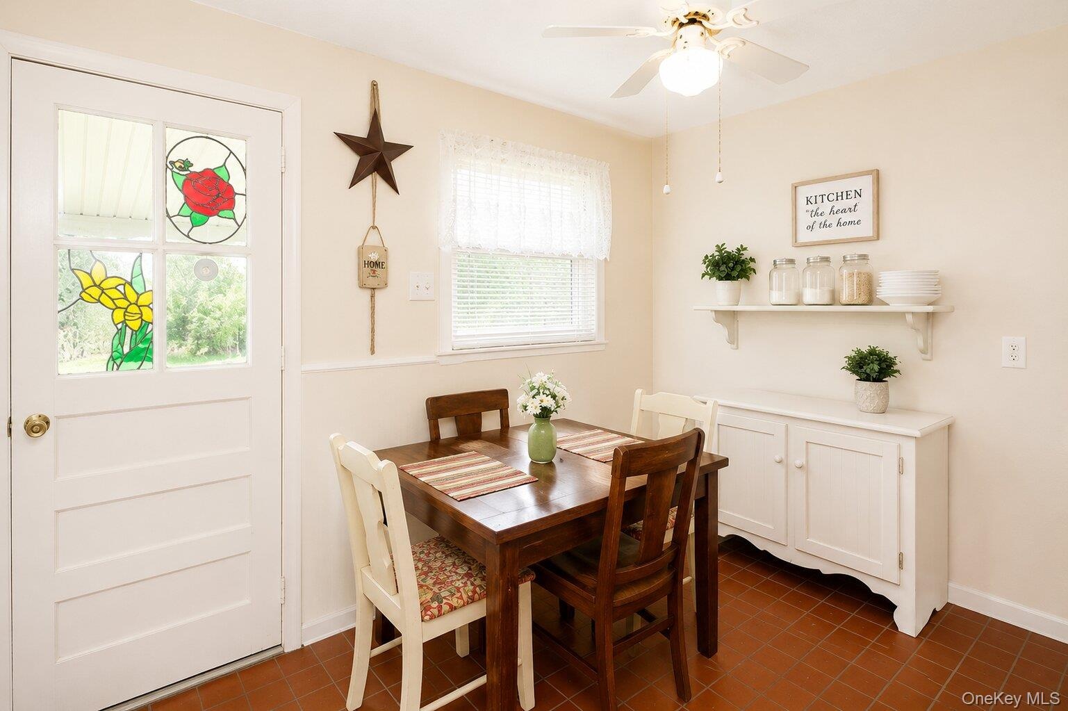 Dining area featuring terracotta-style tile flooring, a built-in white cabinet, and a wall-mounted shelving unit