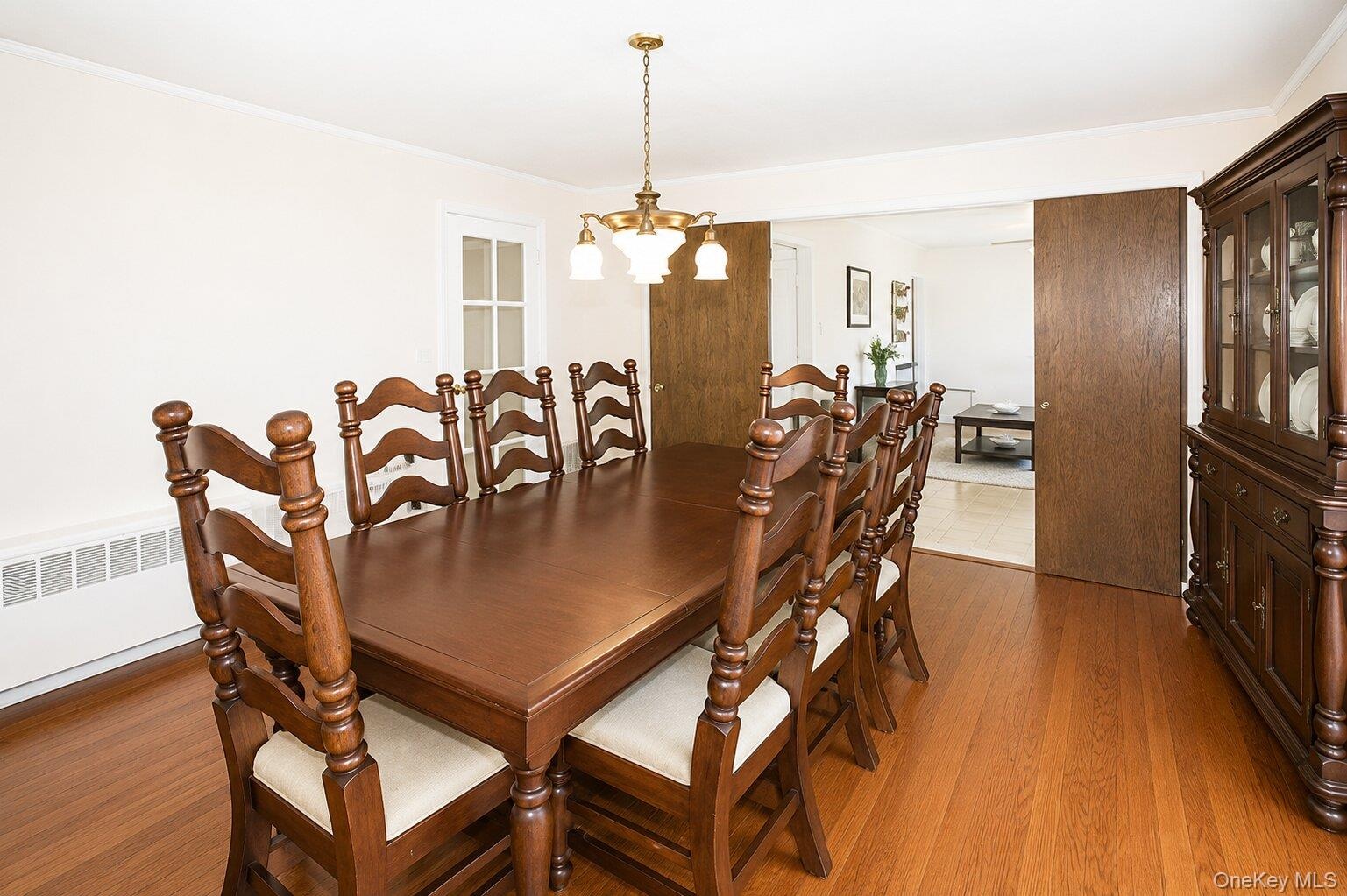Hardwood flooring extends throughout this room, featuring a classic chandelier, crown molding, and a solid wood door frame
