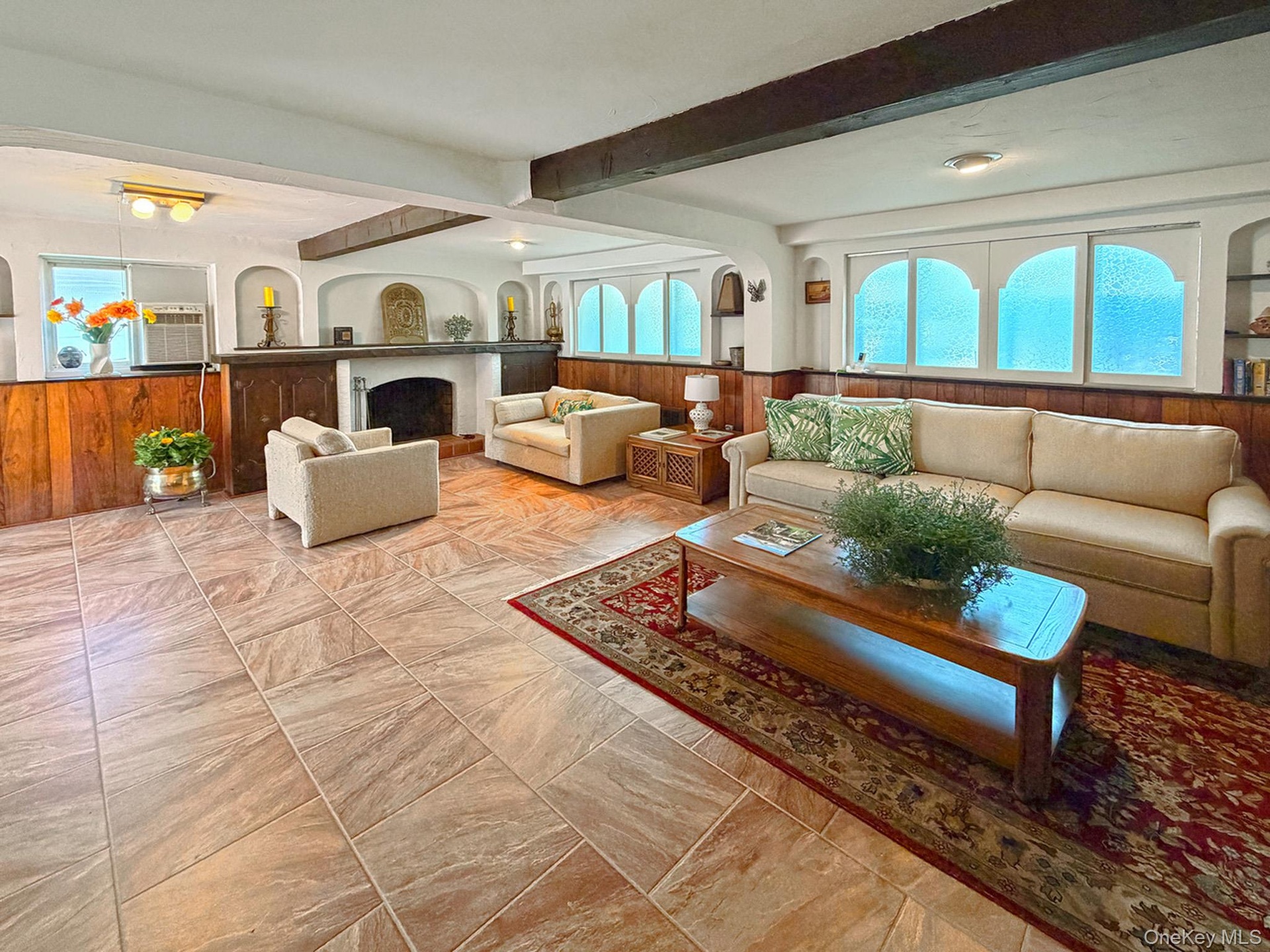 Spacious room featuring tile flooring, exposed wood ceiling beams, a WBFPL and wood paneling on lower walls