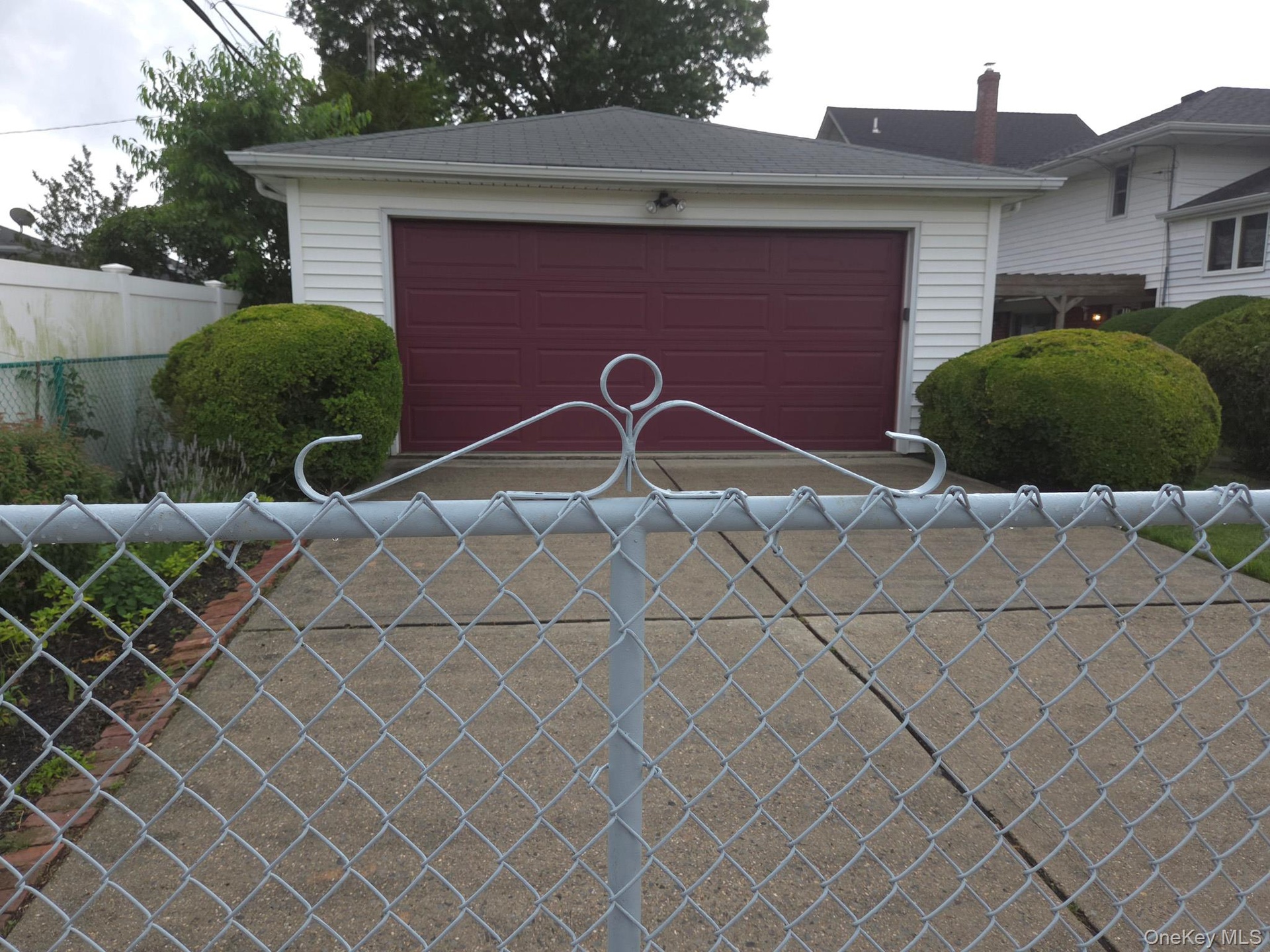 Detached and gated 2 car garage featuring white horizontal siding, a dark red garage door, dark red side door and gabled roof