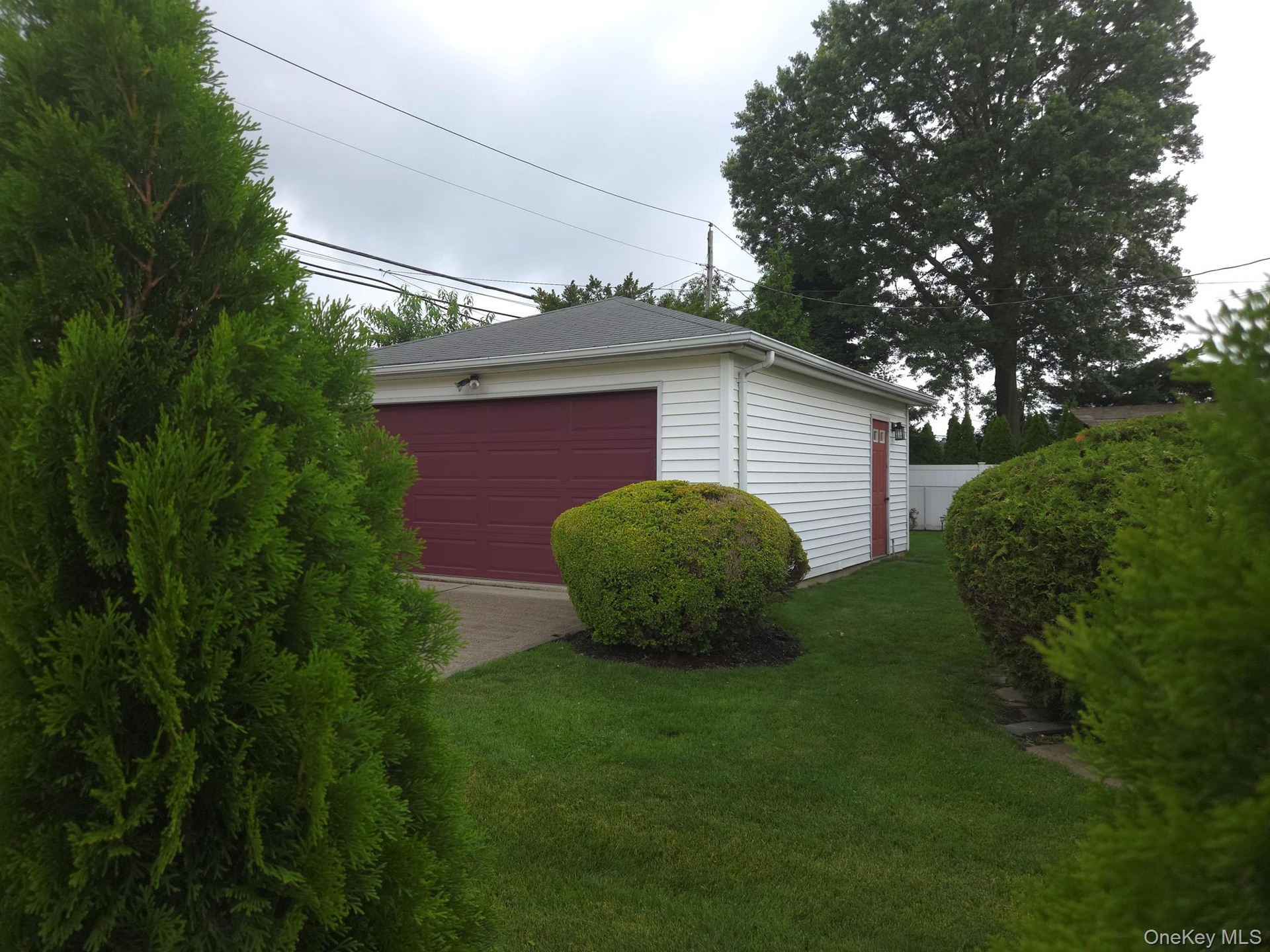 Detached 2 car garage featuring white horizontal siding, a dark red garage door, and a coordinating dark red side door